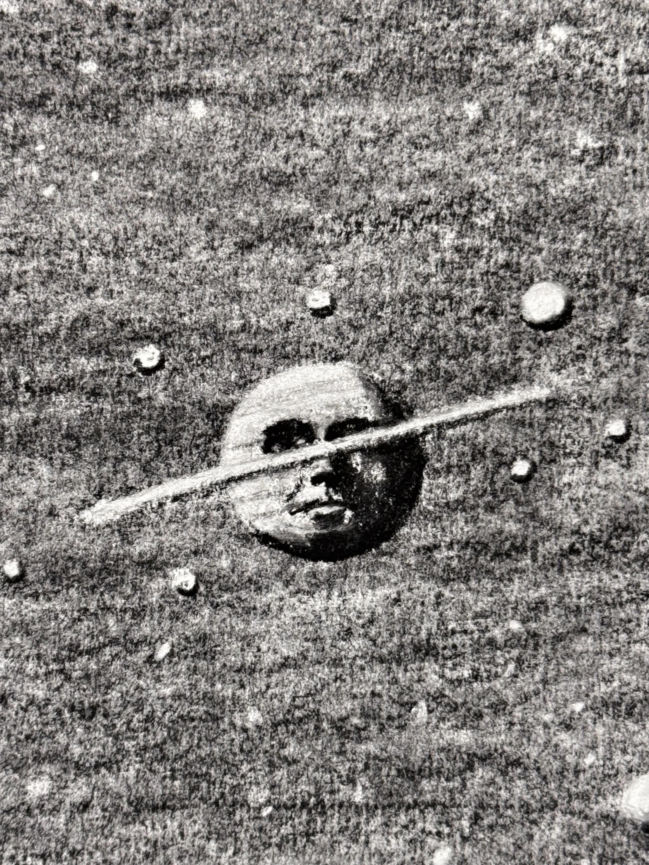 Close up detail of a ringed planet face in Celestial Reverie, a surreal charcoal illustration blending celestial imagery with human expression.