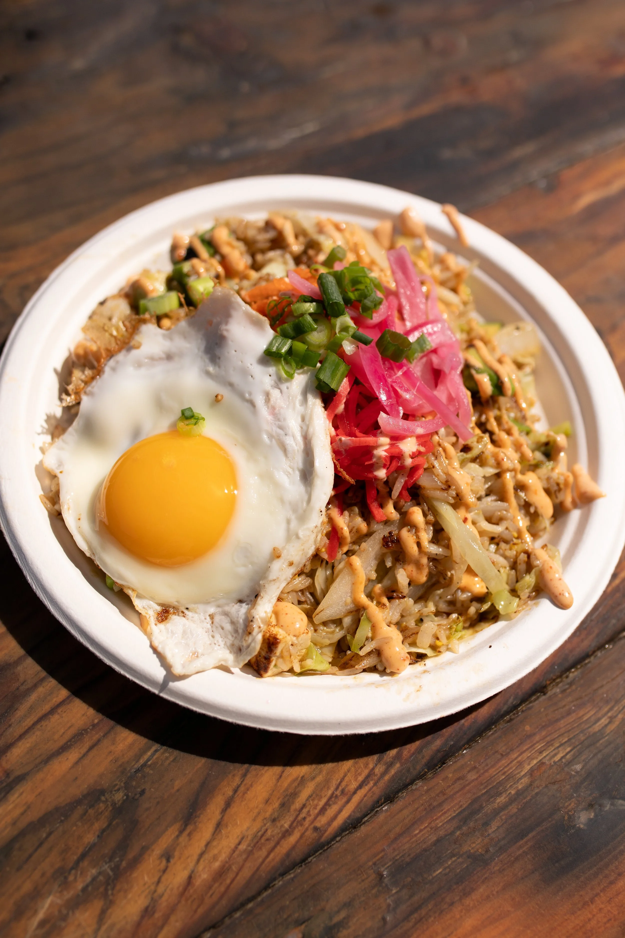 A plate of fried rice topped with a sunny side up egg, garnished with chopped green onions, pickled red onions, and chopped carrots.