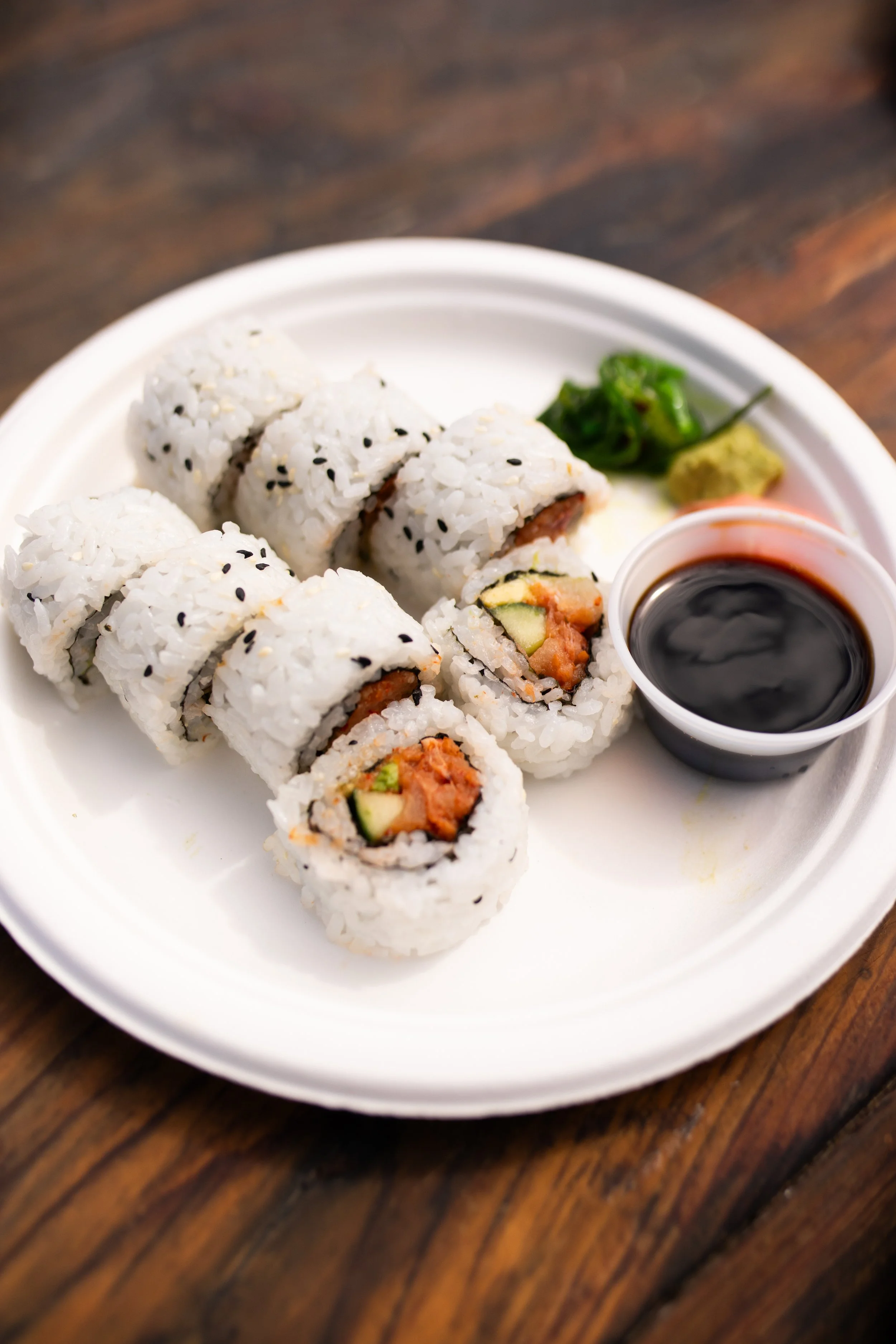 Sushi rolls with soy sauce, wasabi, and pickled ginger on a white paper plate.