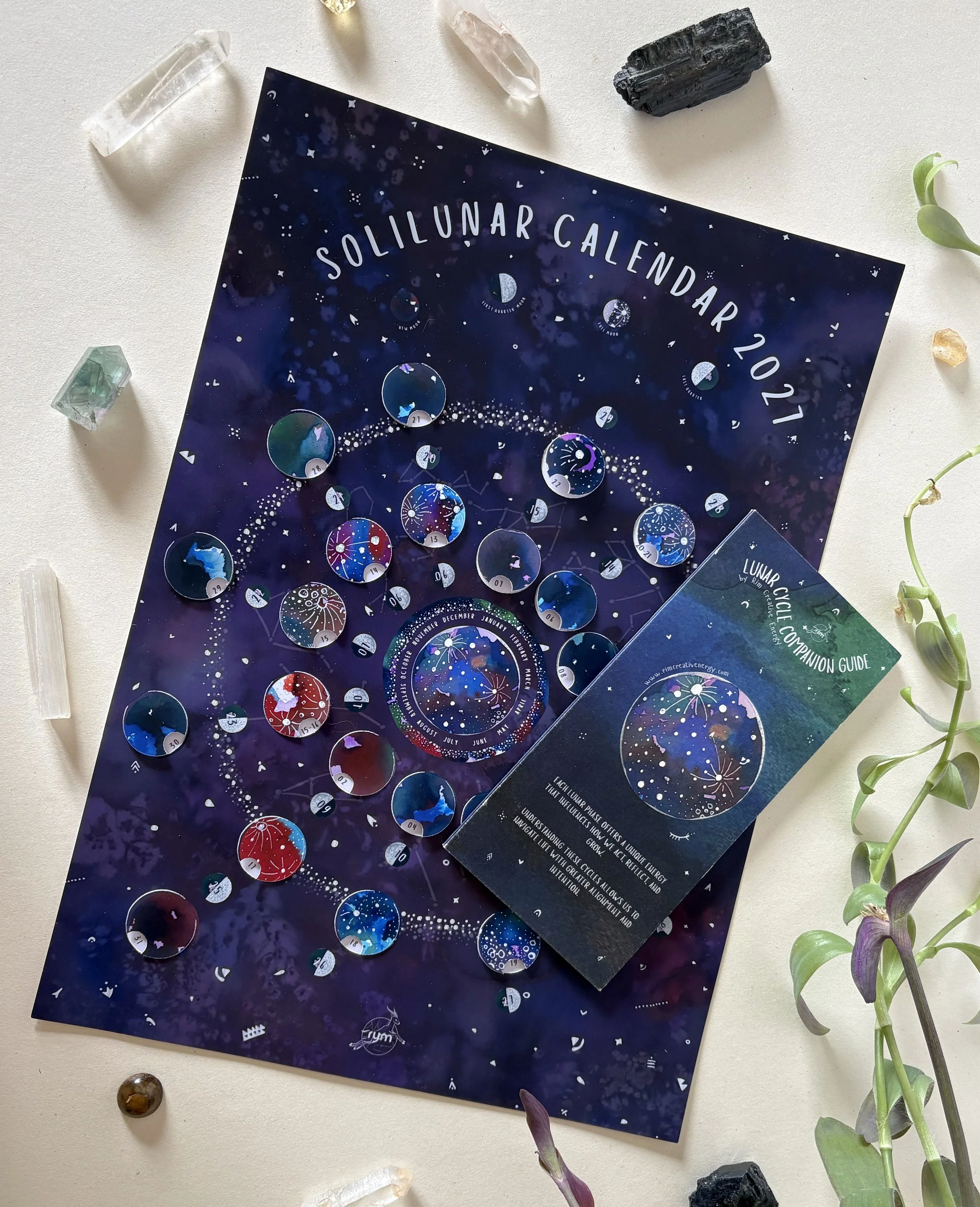 Flatlay of the 2027 Moon Calendar alongside the Moon Companion Guide, showing the matching lunar-themed designs and printed materials.