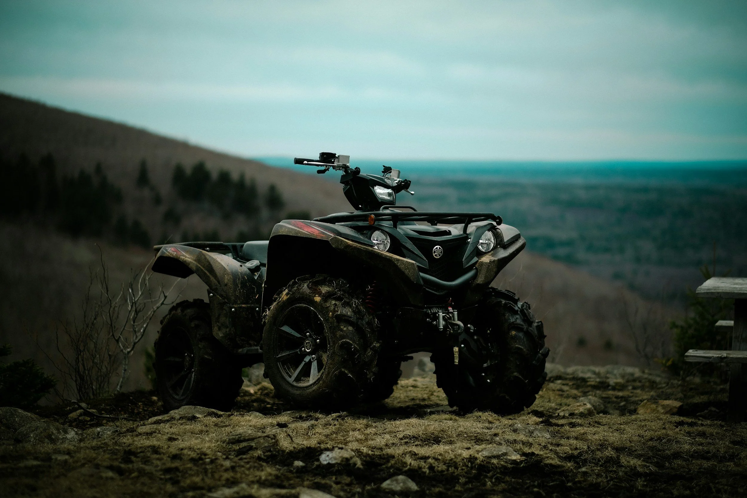 Black Yamaha all-terrain vehicle (ATV) on a dirt patch with a mountainous landscape and cloudy sky in the background.
