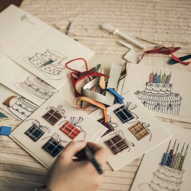 Designer Ana Del Rio's hands drawing her handmade leather greeting cards. The drawings are one-of-a-kind, some are four presents and some are birthday cakes. They have an addition of colour through cut out leather offcut candles and boxes.