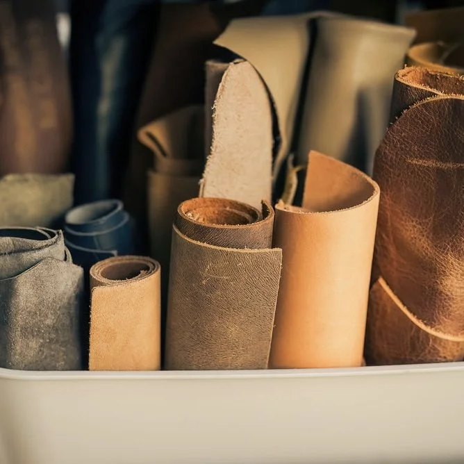 Close-up in Ana Del Rio's studio of bucket of rolled up leathers in natural earthy tones standing upright.