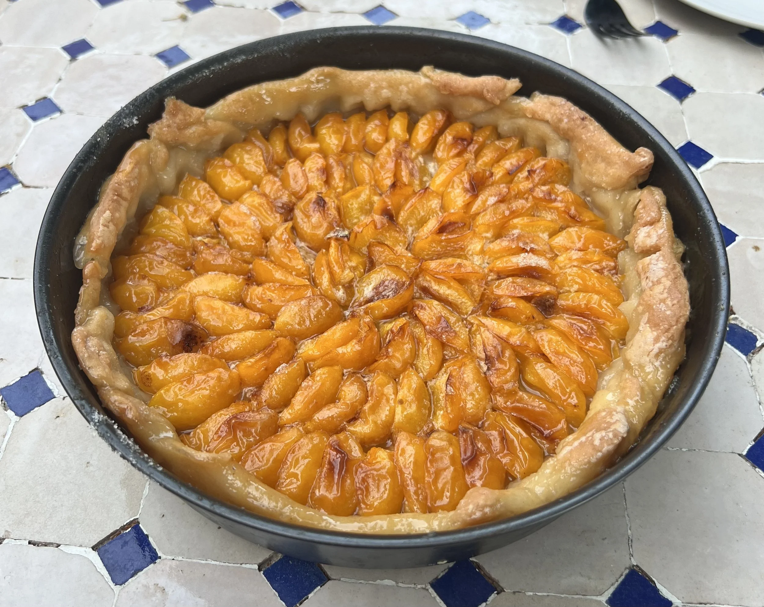 A plum tart with sliced peaches arranged in a circular pattern inside a pie crust in a black baking dish.