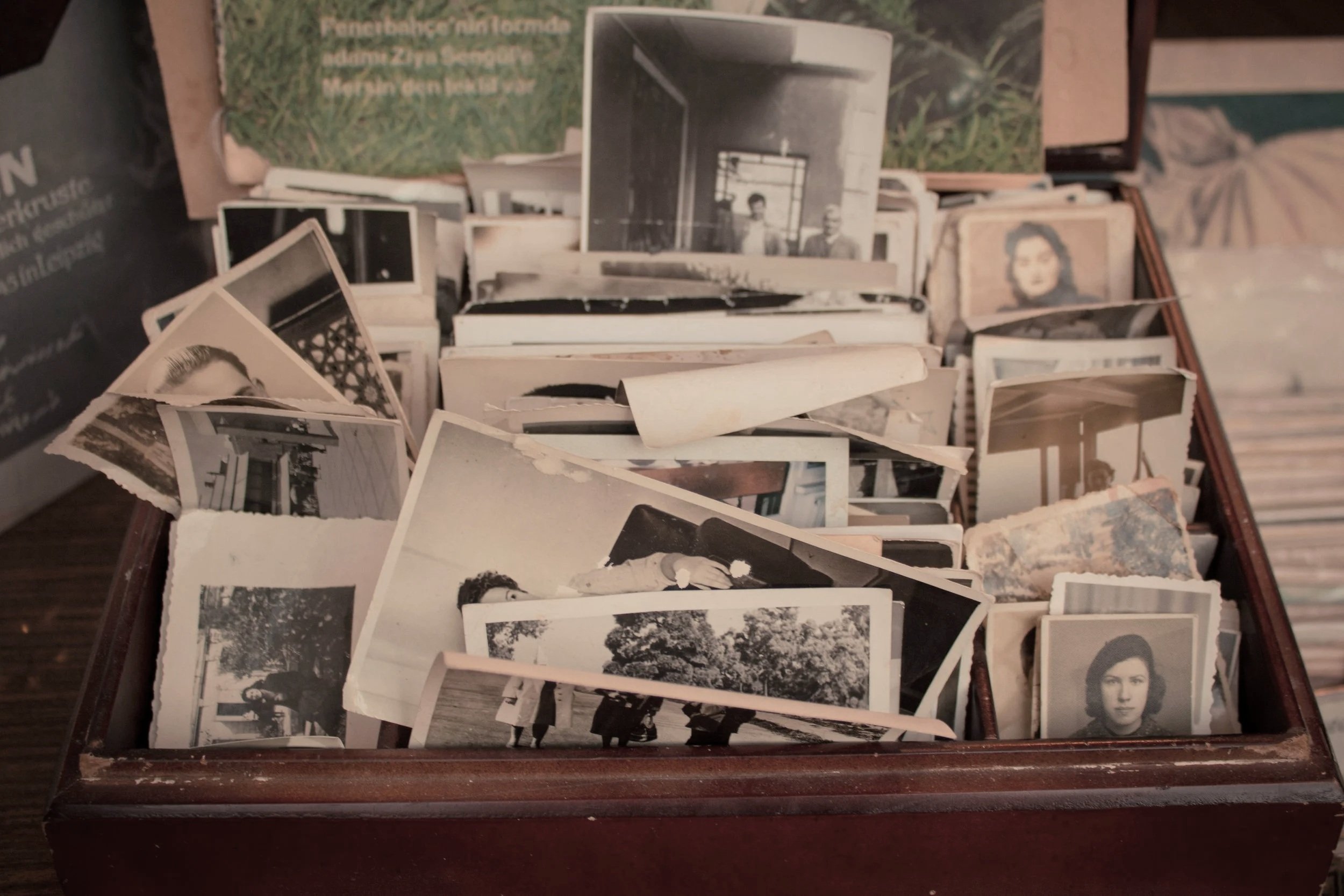 A wooden box filled with black-and-white vintage photographs, with some photos showing people, landscapes, and indoor scenes, arranged in a slightly chaotic manner.