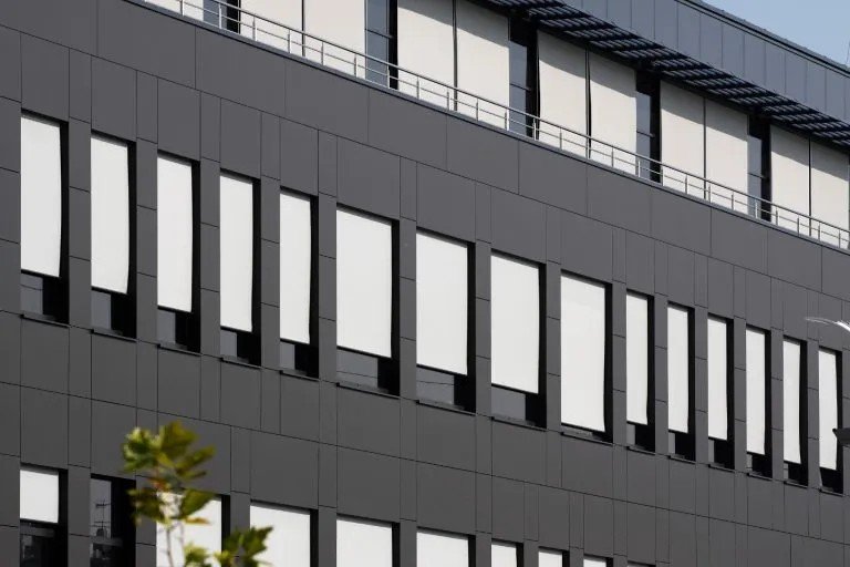 Fasade av en moderne bygning med mørke veggpaneler og mange vinduer