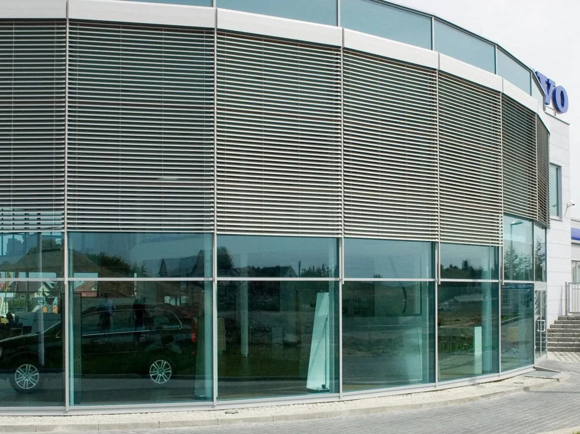 Fasade av en moderne bygning med store glassvinduer og luftige metalllameller