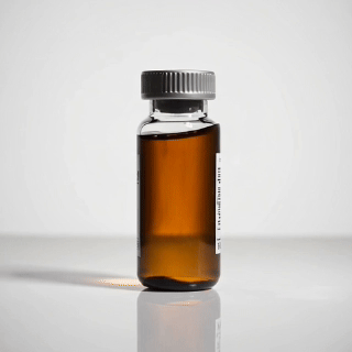 Pequeño frasco de vidrio marrón con tapón gris, probablemente conteniendo un líquido oscuro, sobre una superficie blanca.