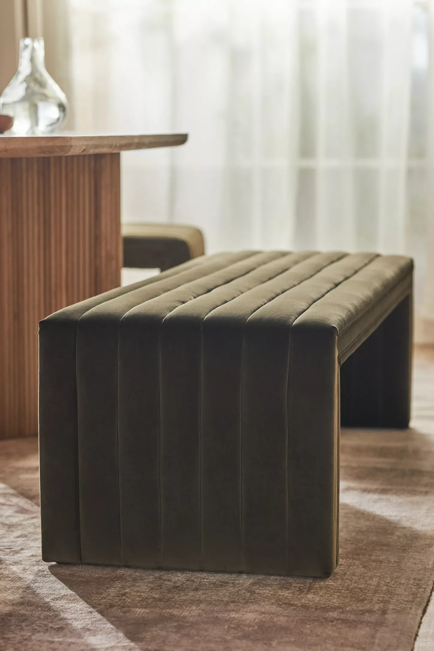 An olive green colored velvet bench with channel detailing on the upholstery