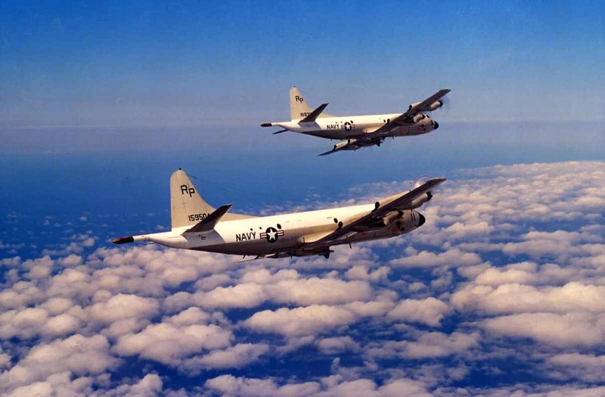 Two military aircraft flying above a layer of clouds in the sky.