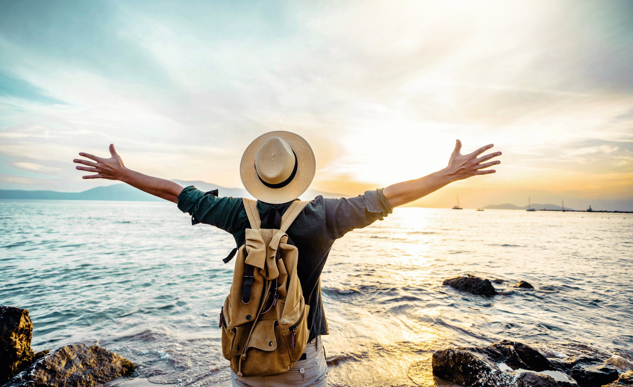 Picture of man at sunset with arms outsttretched facing the ocean.