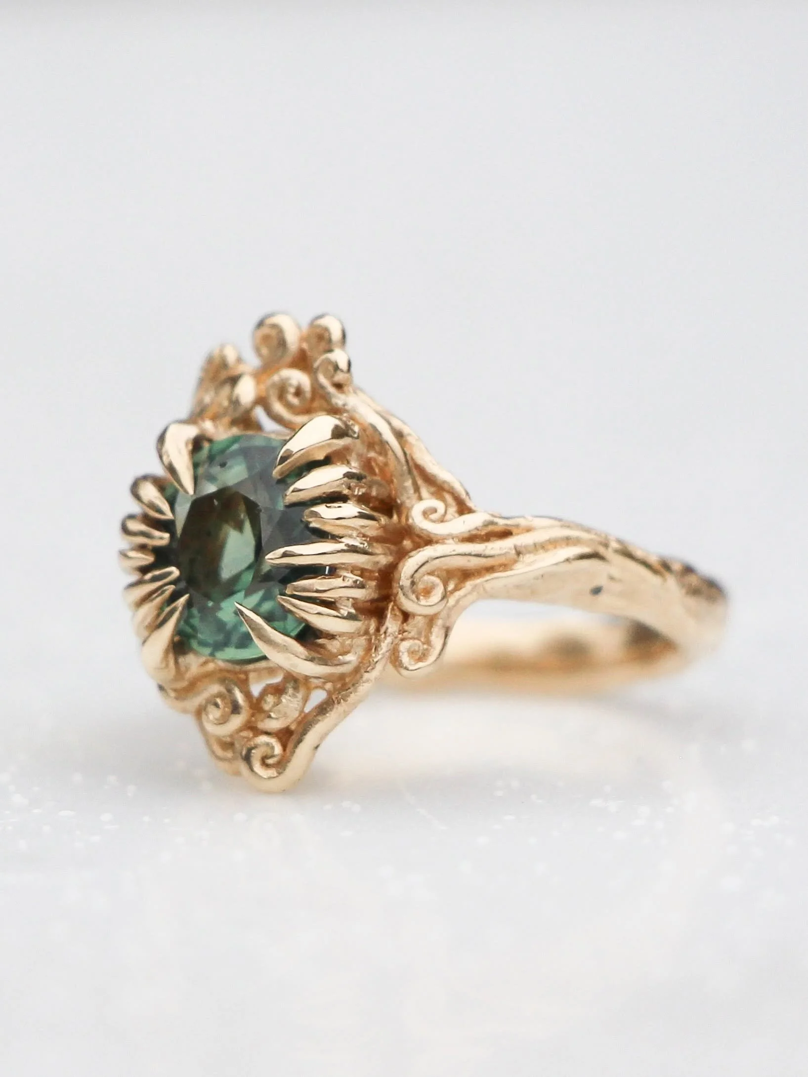 Close-up of a gold ring with a large green gemstone and intricate scrolling design on a white background.