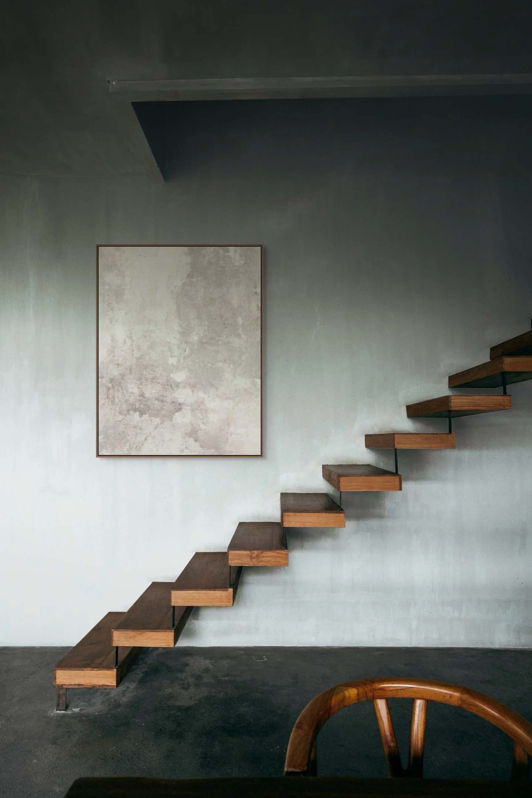 Modern interior with a floating wooden staircase, abstract artwork on the wall, and a wooden chair partially visible in the foreground.