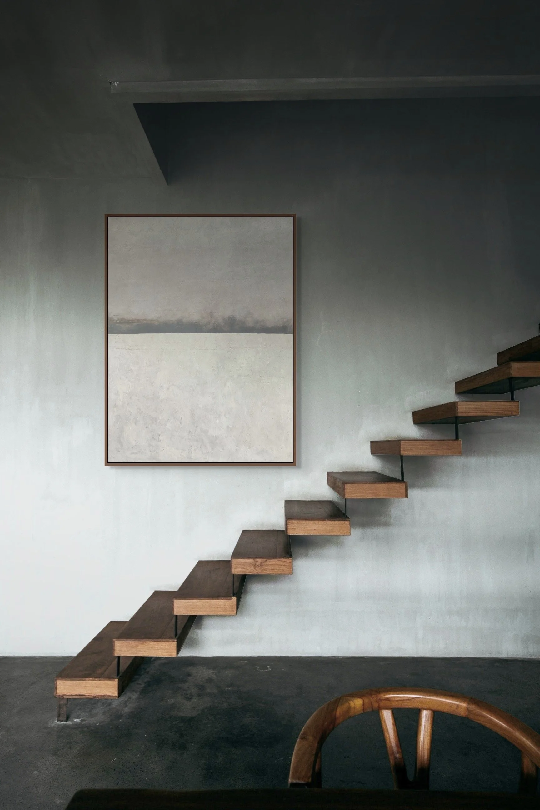 Interior of a modern home with a minimalist staircase made of wooden steps and black supports, a large abstract painting on a gray wall, and a wooden dining chair in the foreground.
