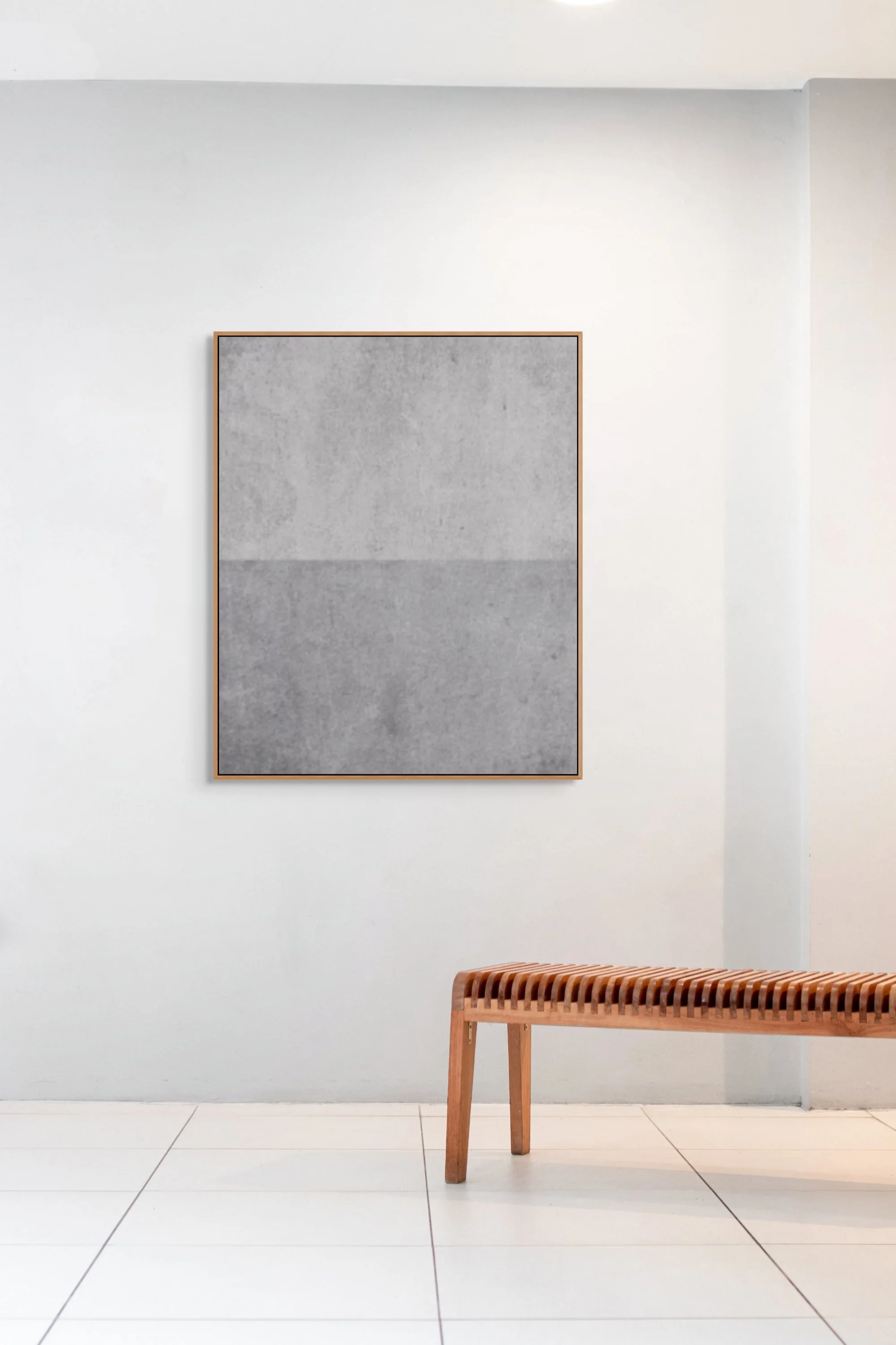 Minimalist room with a white wall, a large abstract gray artwork, and a wooden bench with a slatted seat.