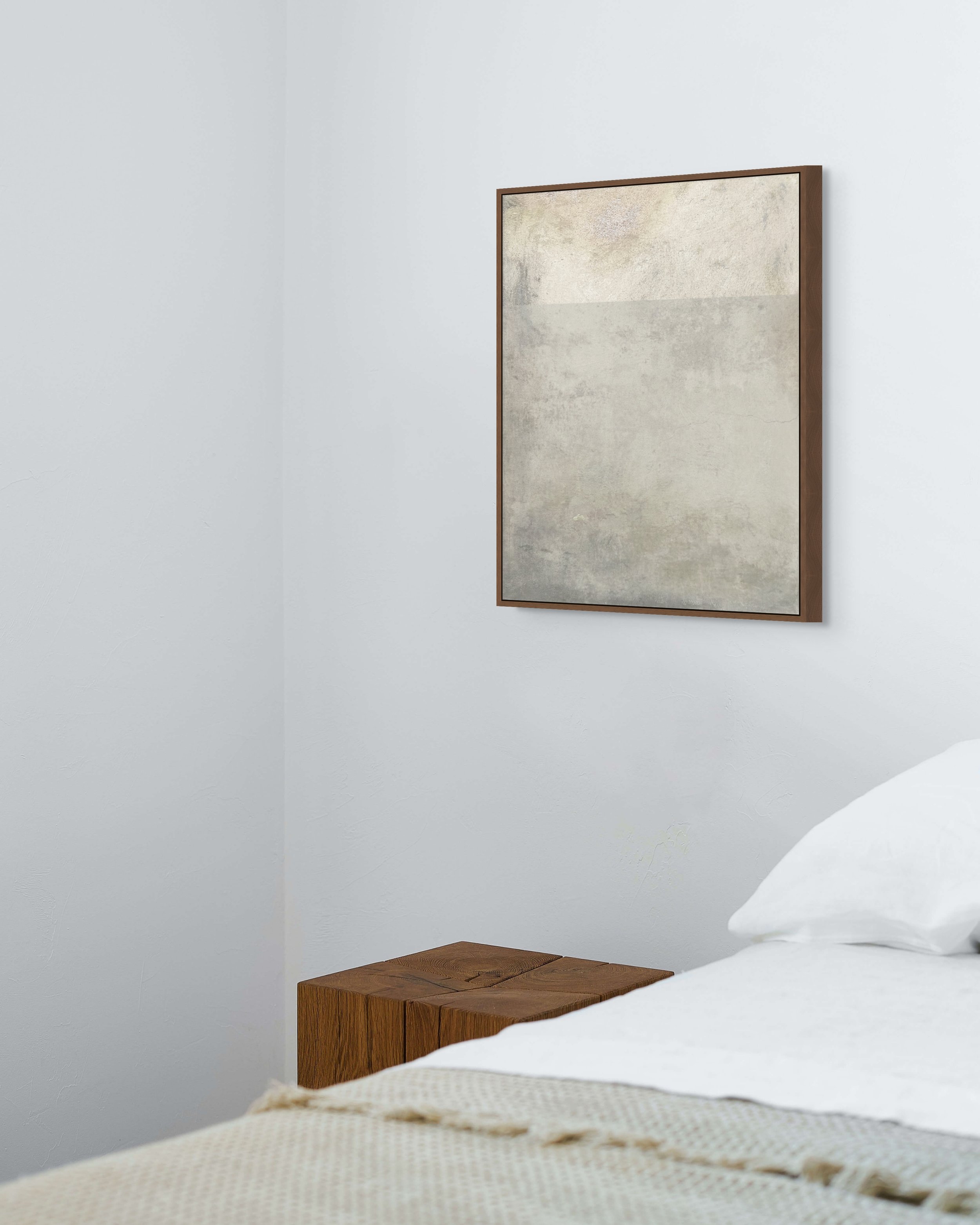 A bedroom corner with a wooden bedside table, a bed with white sheets, and a framed abstract artwork on a white wall.