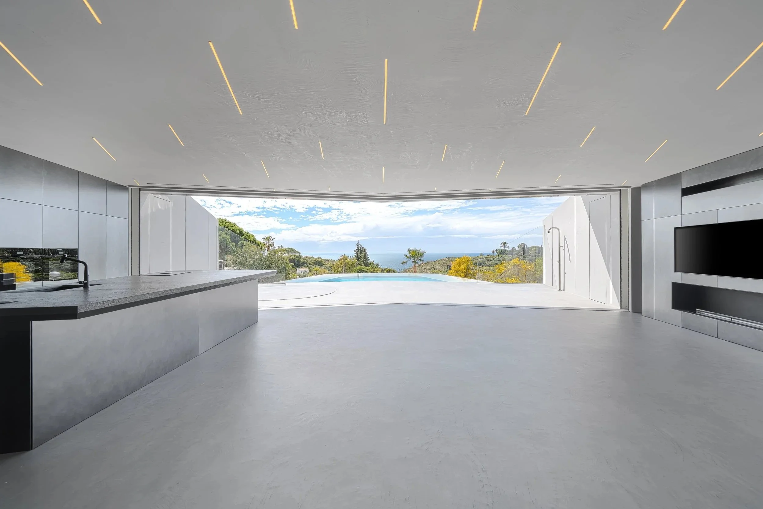 Moderner, offener Raum mit großen Glasfenstern, die eine Aussicht auf eine Landschaft mit Bäumen, Hügeln und den Himmel bieten, und einem Pool im Freien.