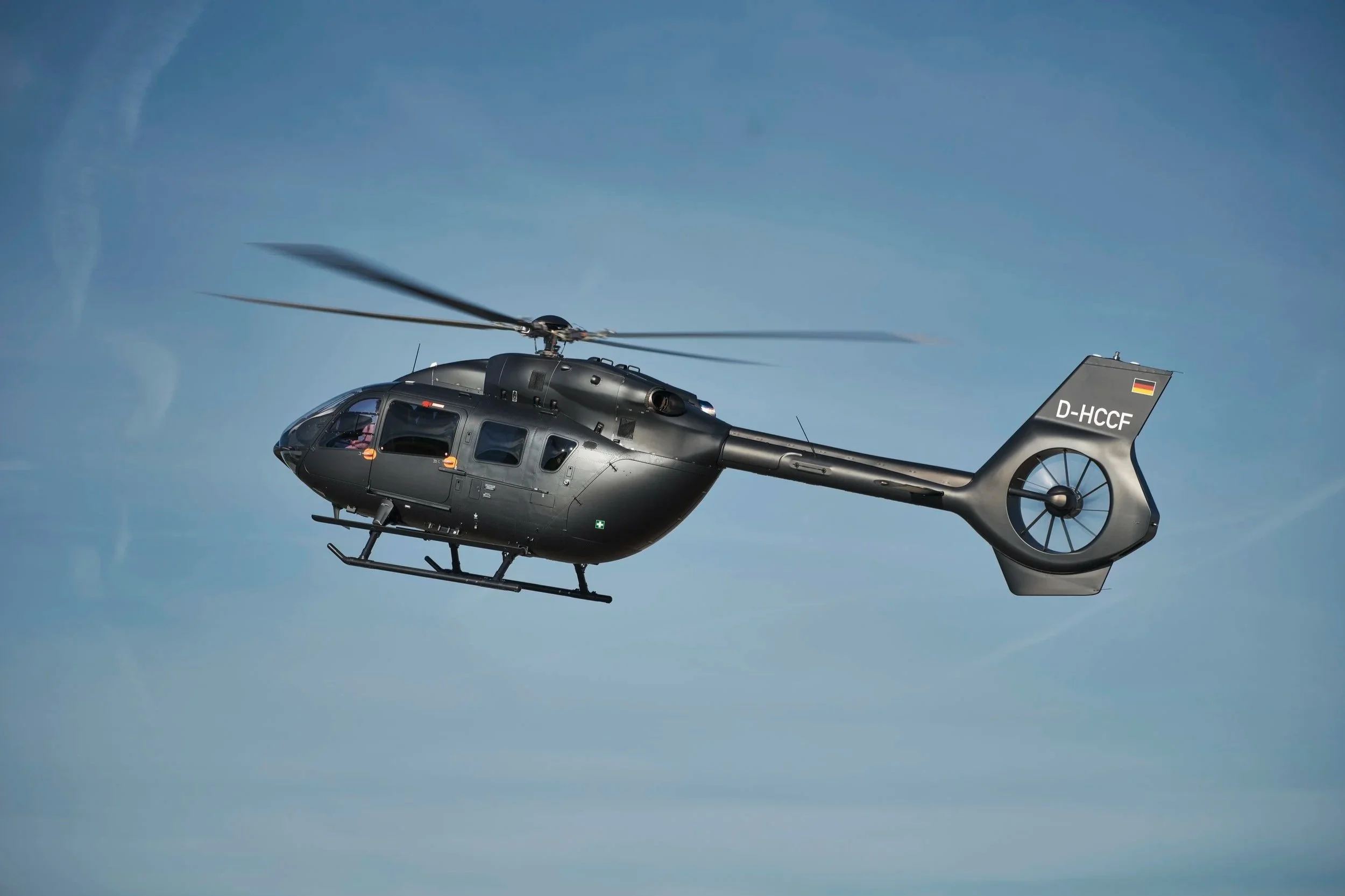 Schwarzer Hubschrauber fliegt bei blauem Himmel.