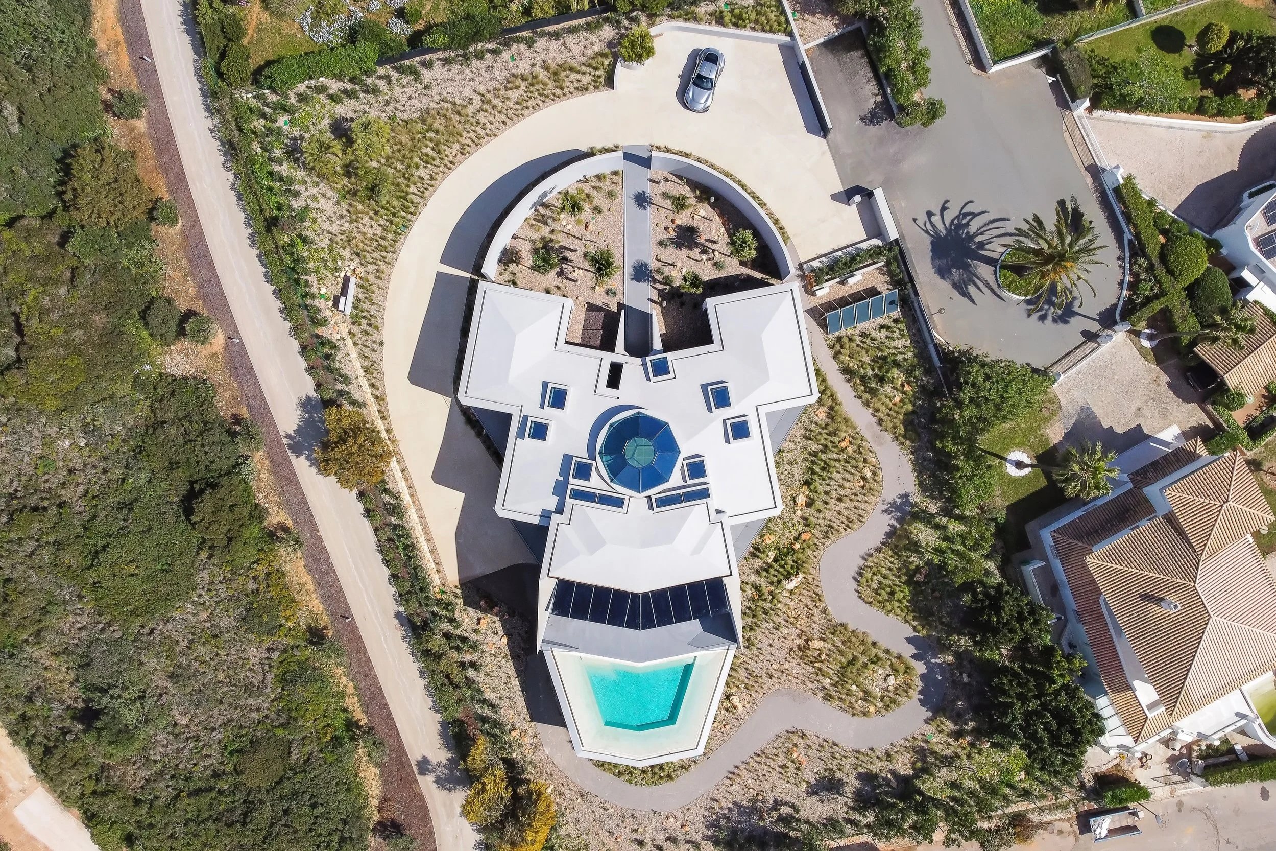 Luftaufnahme eines modernen weißen Hauses mit Swimmingpool, umgeben von Bäumen und Straßen.