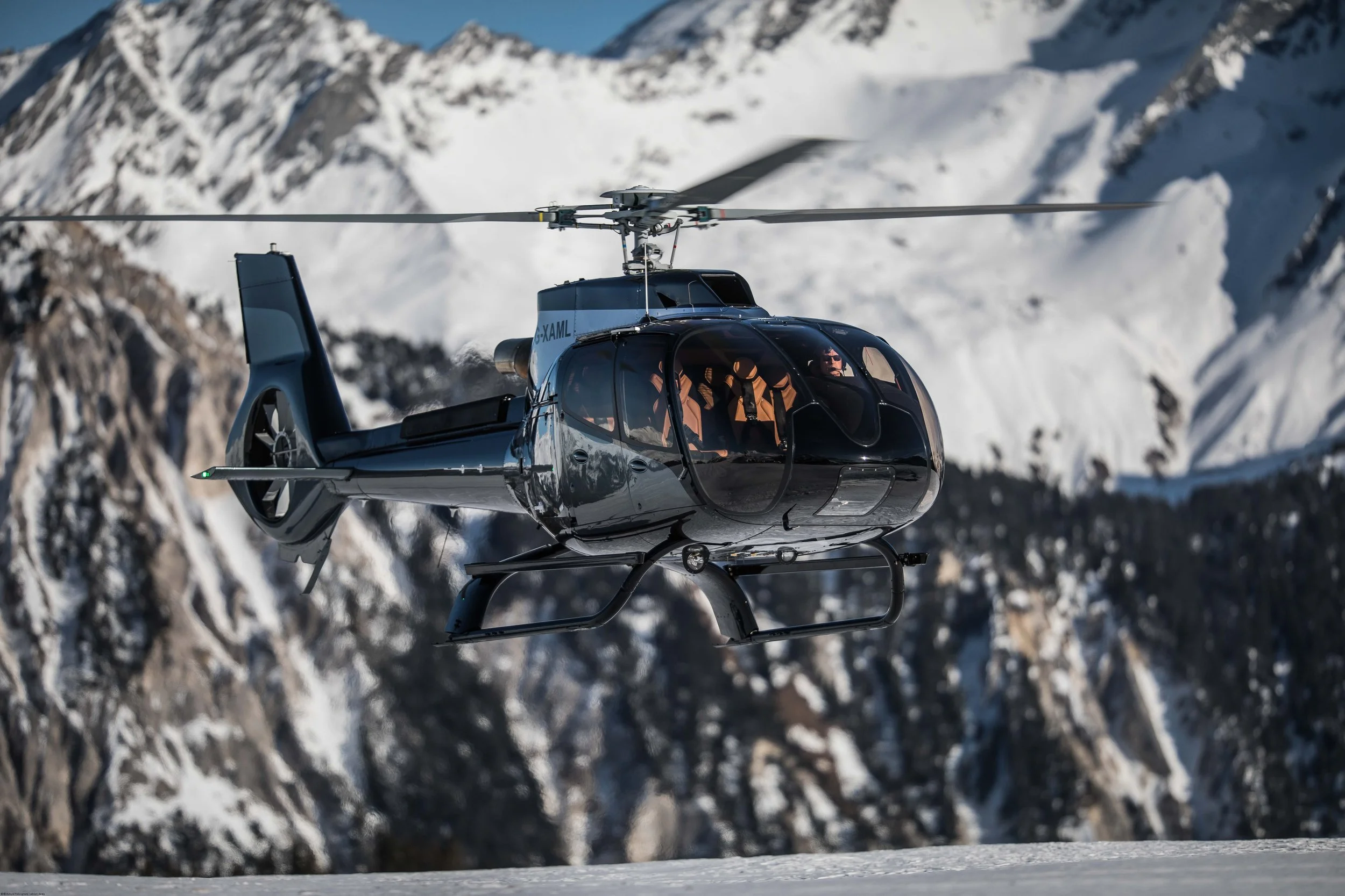 Ein Hubschrauber fliegt über verschneite Berge in einer Berglandschaft.