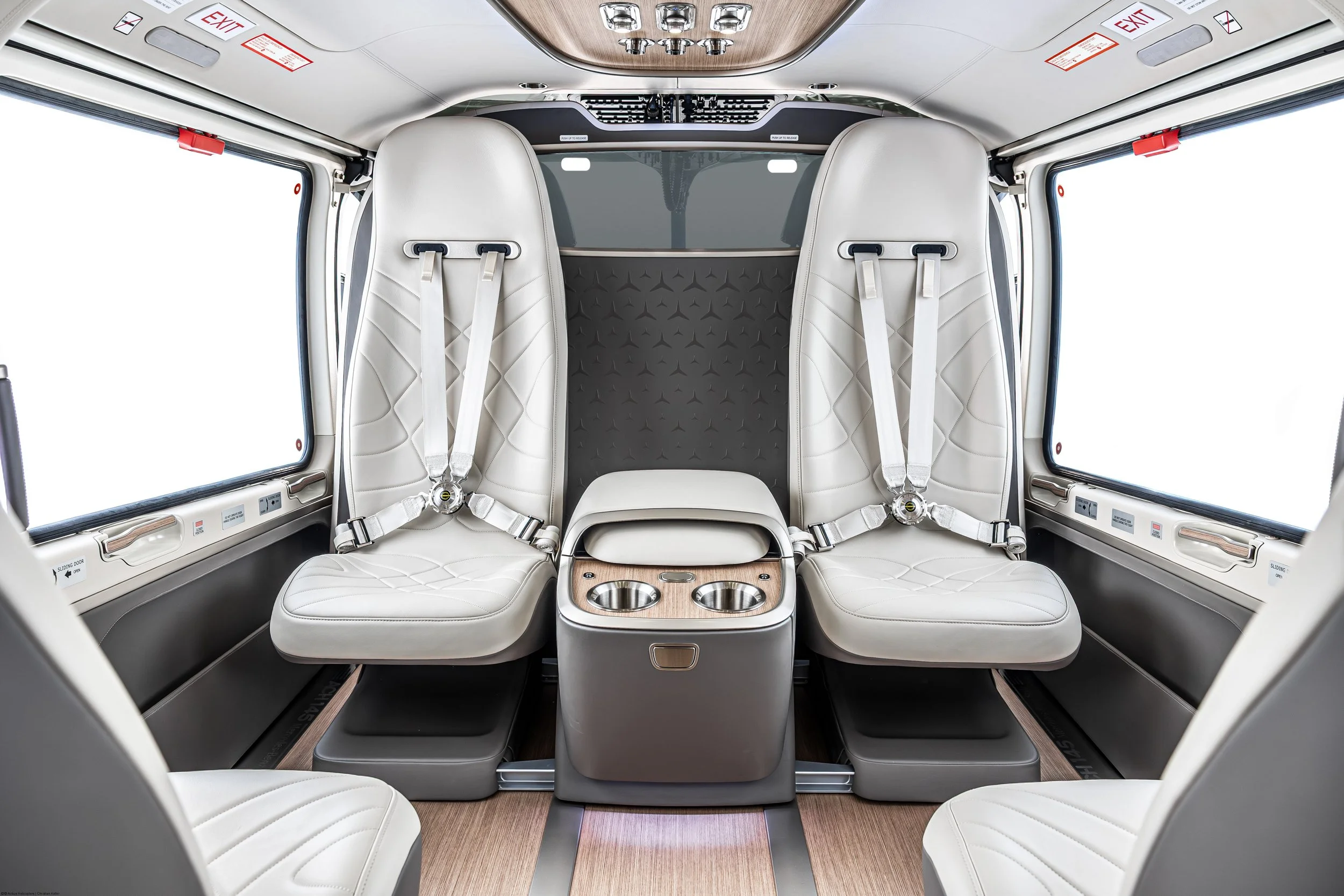 Innenraum eines modernen, eleganten Hubschraubers mit weißen Ledersitzen, großen Fenster und Holzelementen.