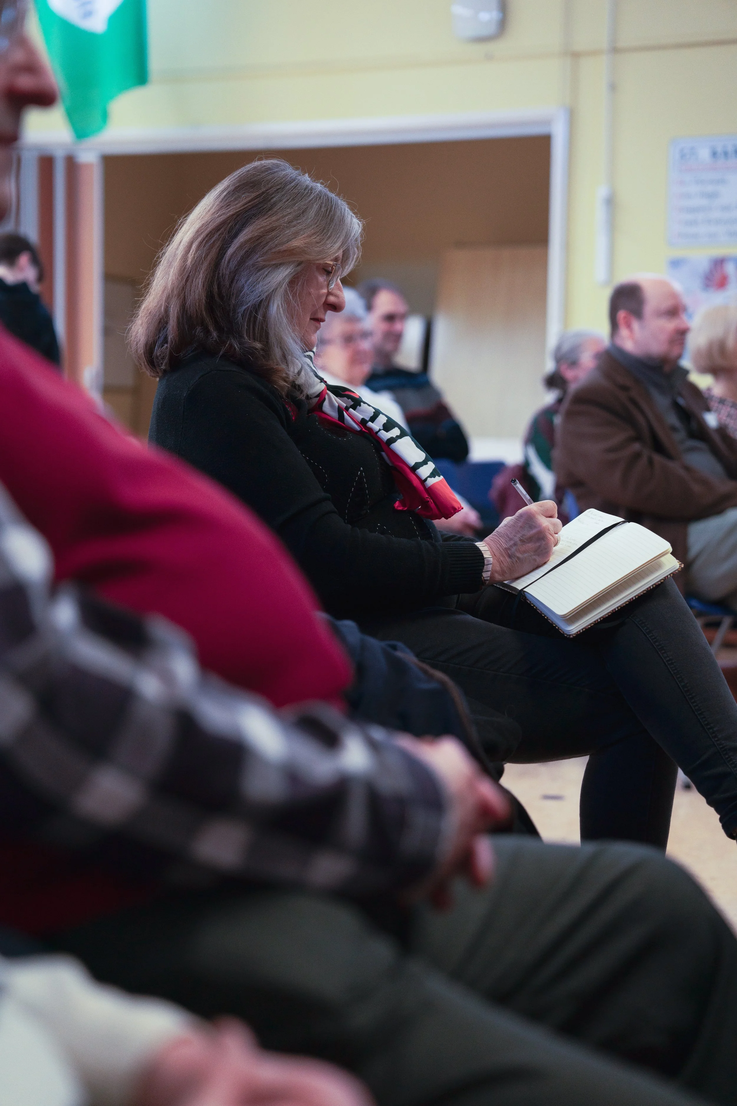 A woman taking notes in a notebook during a meeting or presentation.