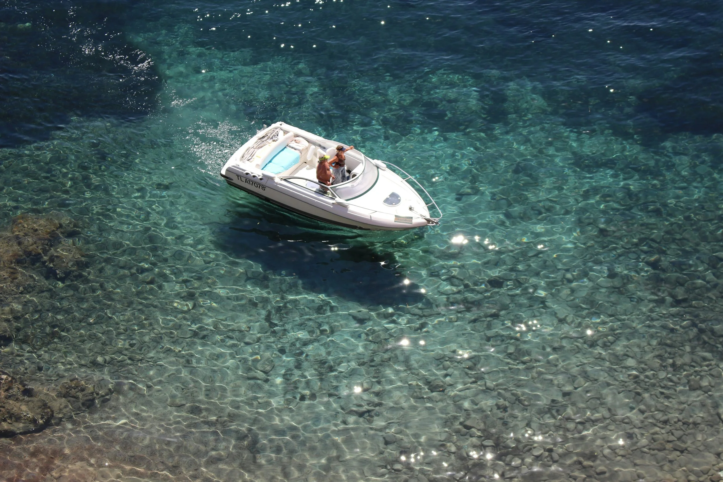 Una barca a motore in acque cristalline con due persone a bordo, una indossa un cappello verde e l'altra indossa un cappello beige, circa a mezzogiorno.