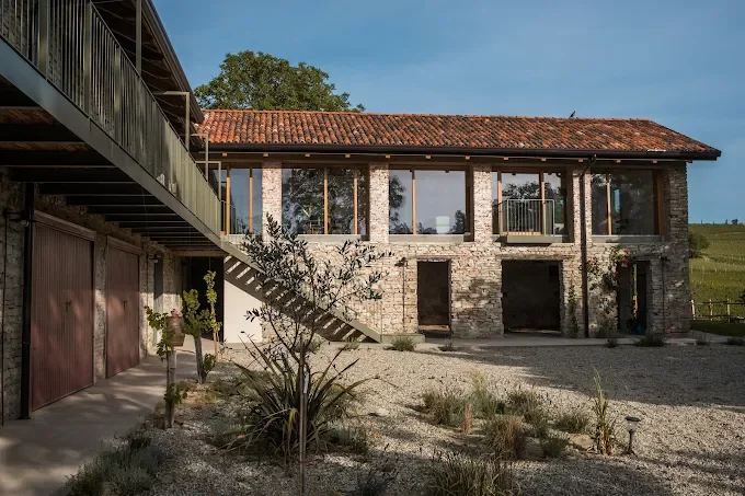 Una casa in costruzione con muri di mattoni e grandi finestre, con un cortile esterno e un deposito garage a sinistra.