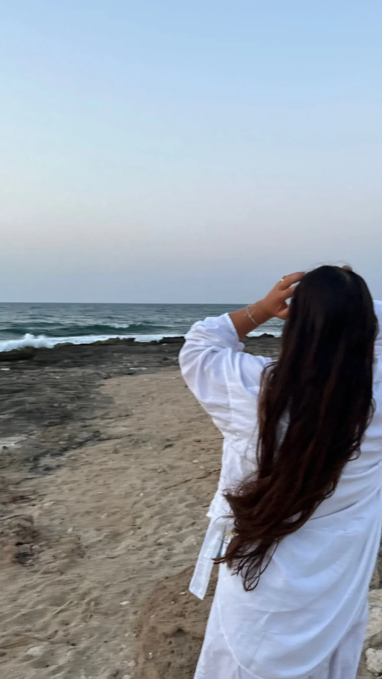 Donna con capelli lunghi guarda il mare sulla spiaggia al tramonto.