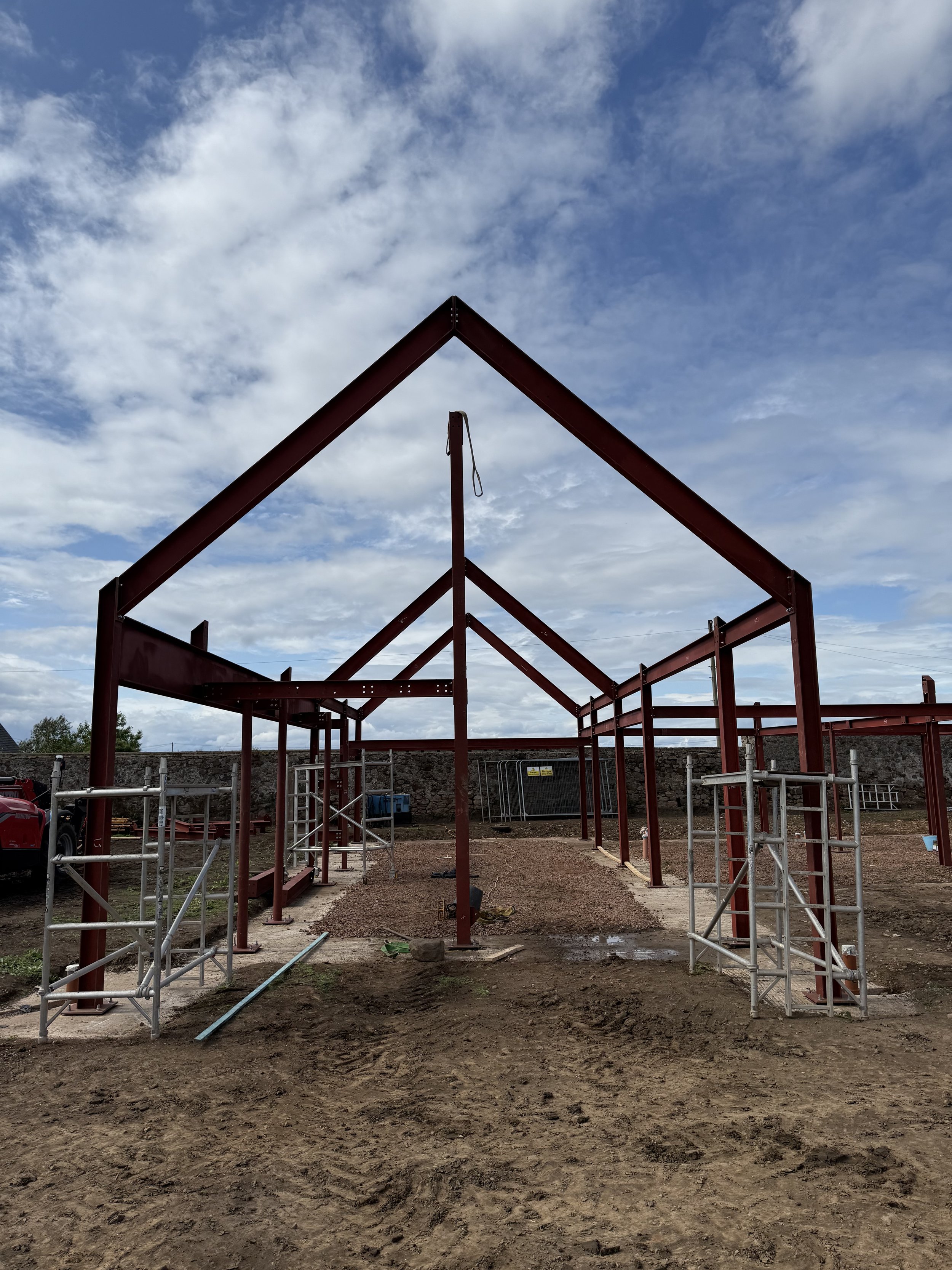 Steel framework building under construction with scaffolding and cloudy sky in the background.