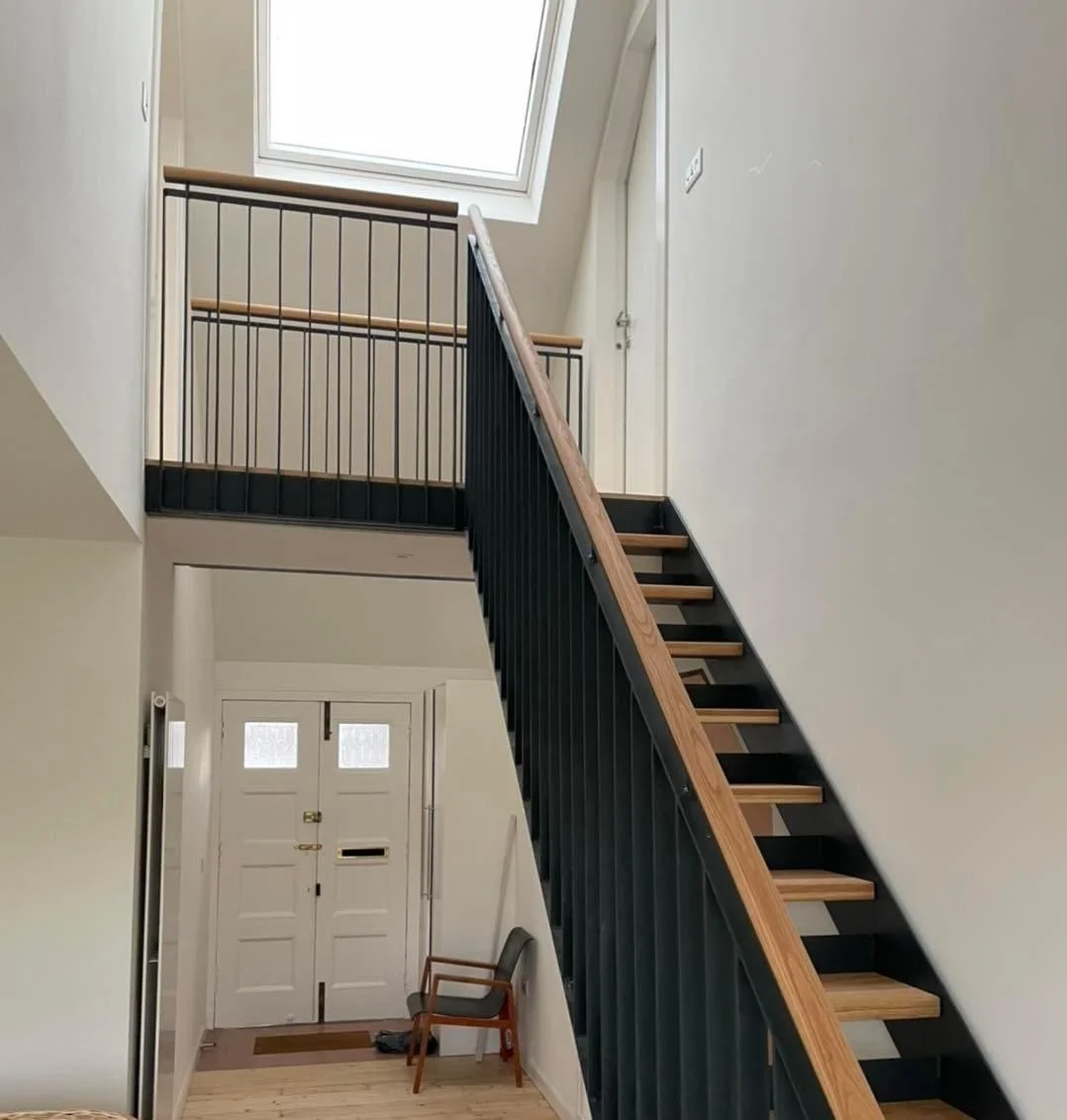 Interior view of a house entryway with double front doors, and a staircase with wooden steps and a black metal railing leading to an upstairs landing.