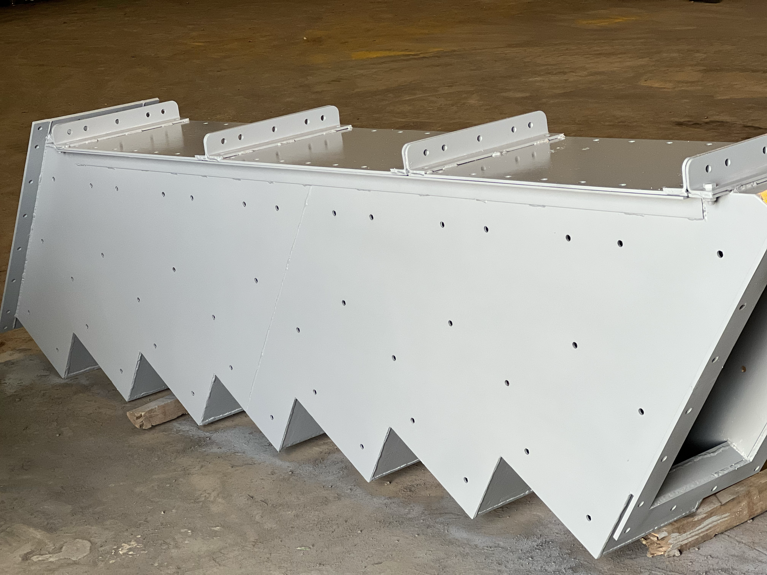 White metal staircases with perforated sheets, leaning against a pile of wood on a concrete floor.