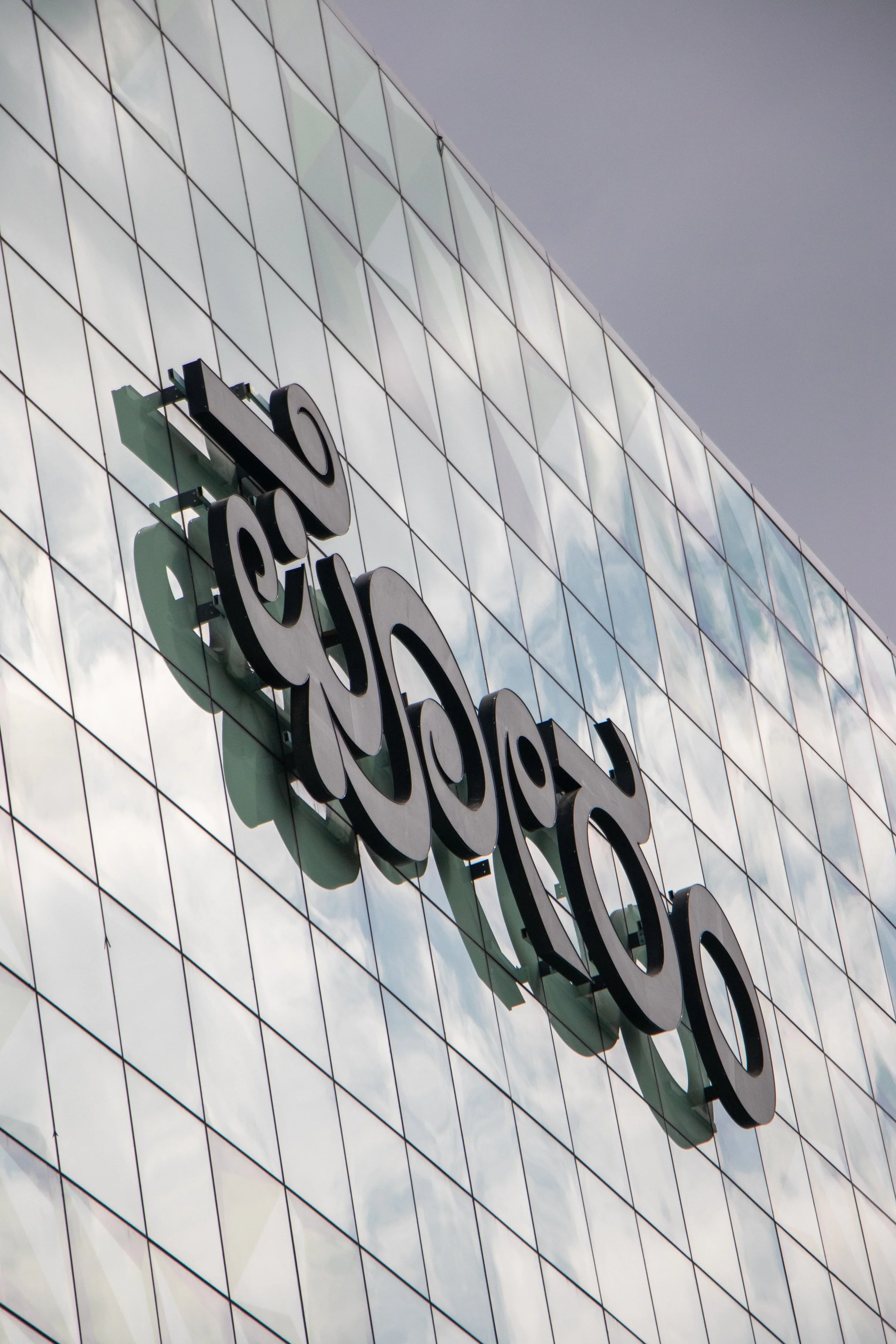 Close-up of the Rotterdam sign on a modern building with reflective glass panels reflecting clouds and the sky.