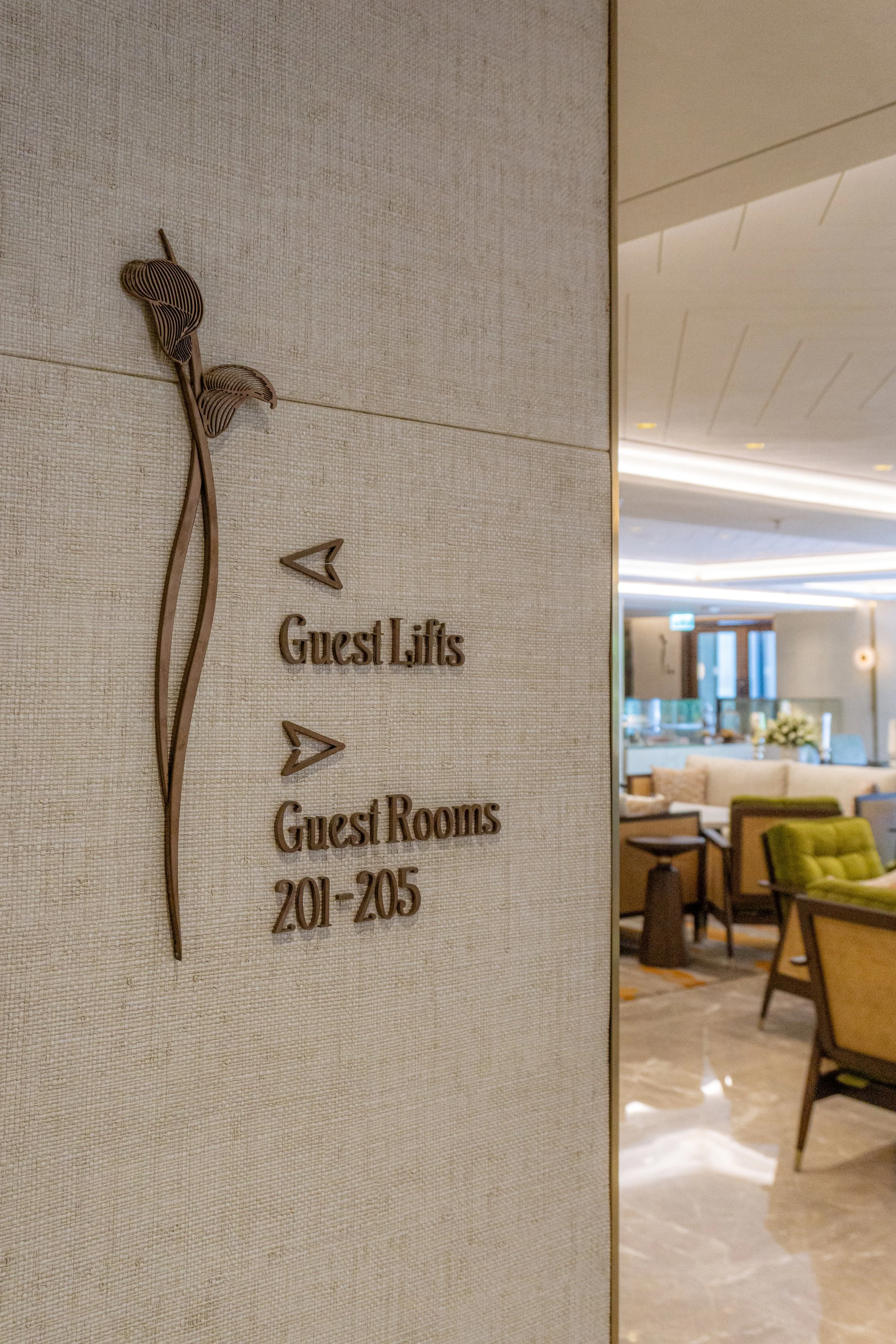 Sign indicating directions to guest lifts and rooms, number range 201 to 205, in a hotel lobby with seating area and modern decor.