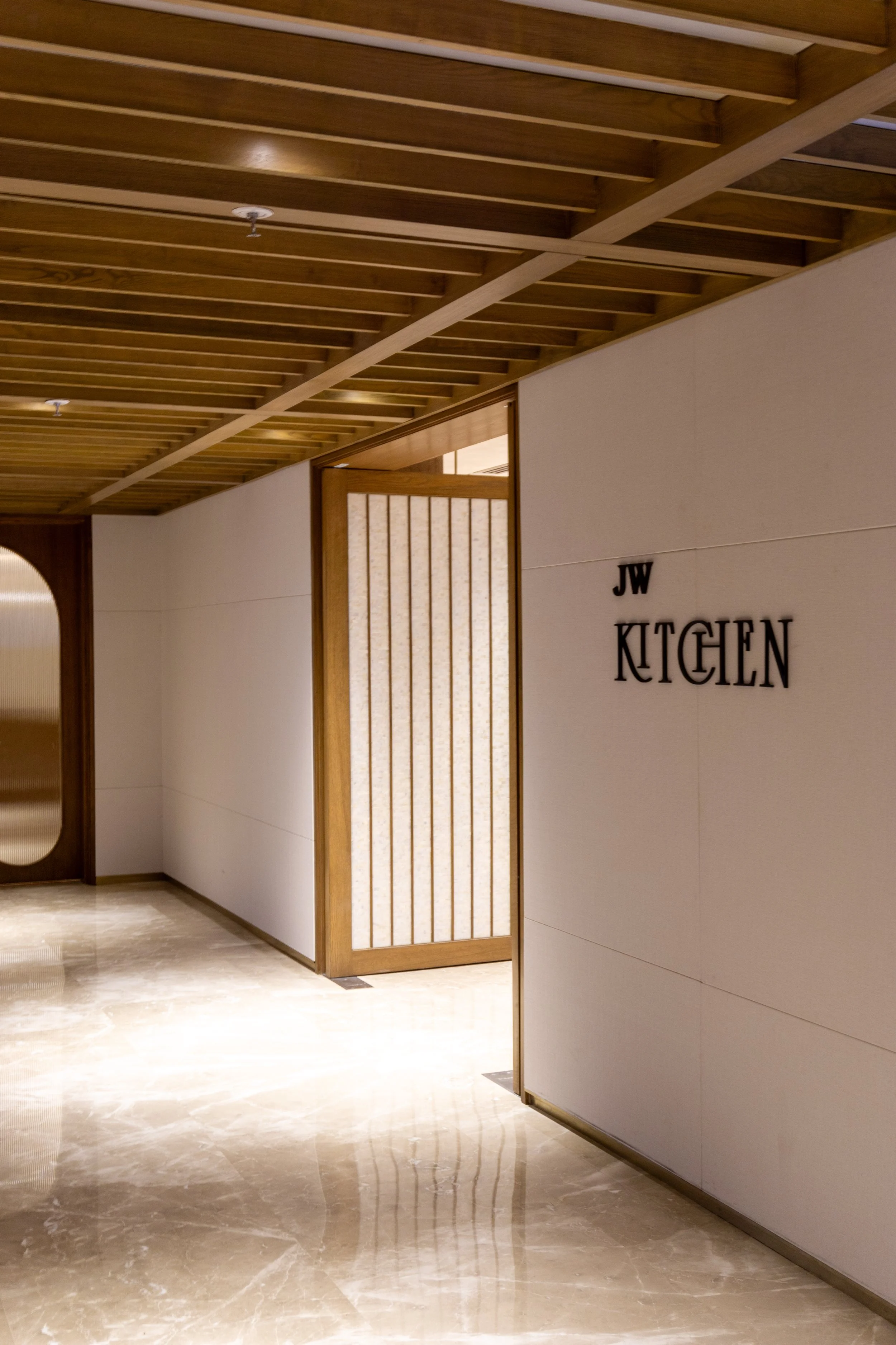 Interior view of JW Kitchen with wooden ceiling, white walls, and polished marble floor.