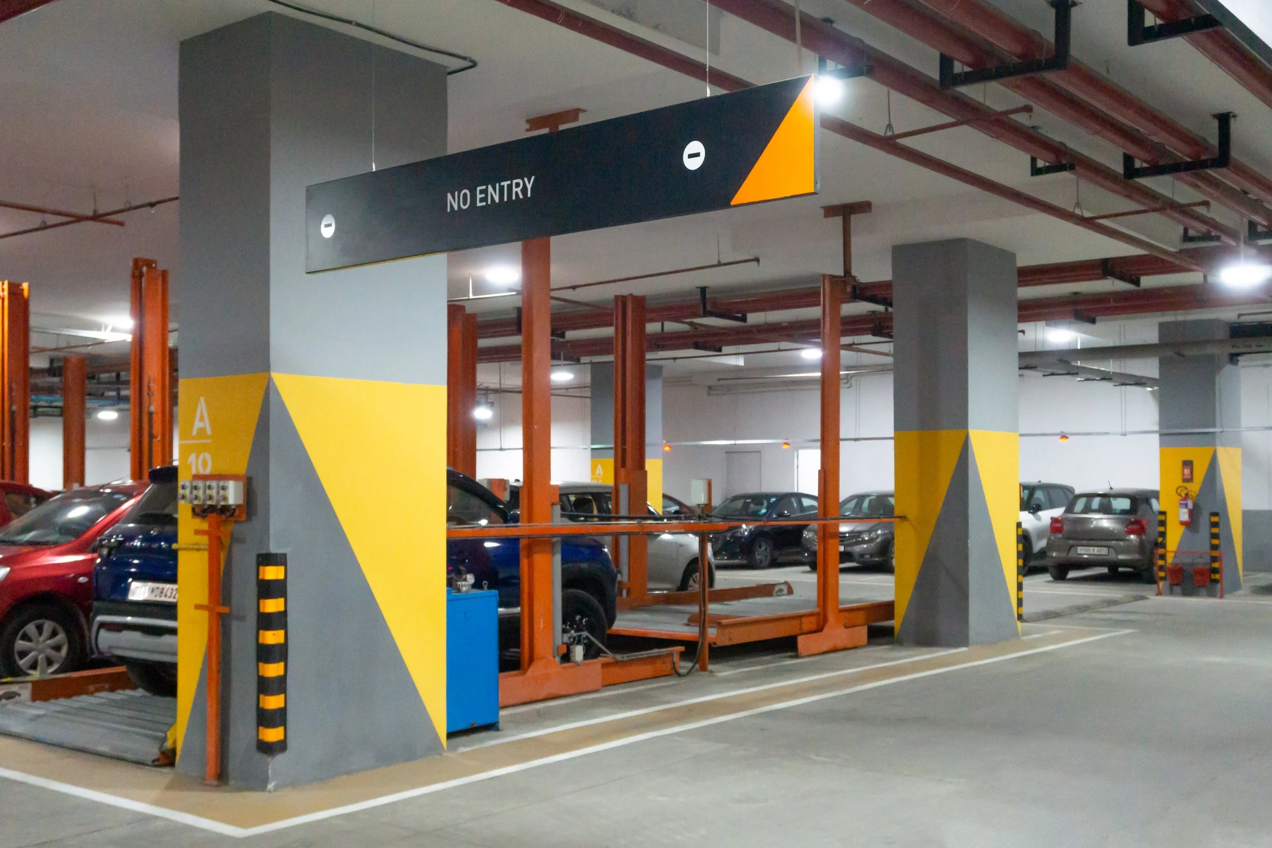 Underground parking garage with parked cars, concrete pillars painted in grey and yellow, and a sign overhead that reads 'No Entry'. 