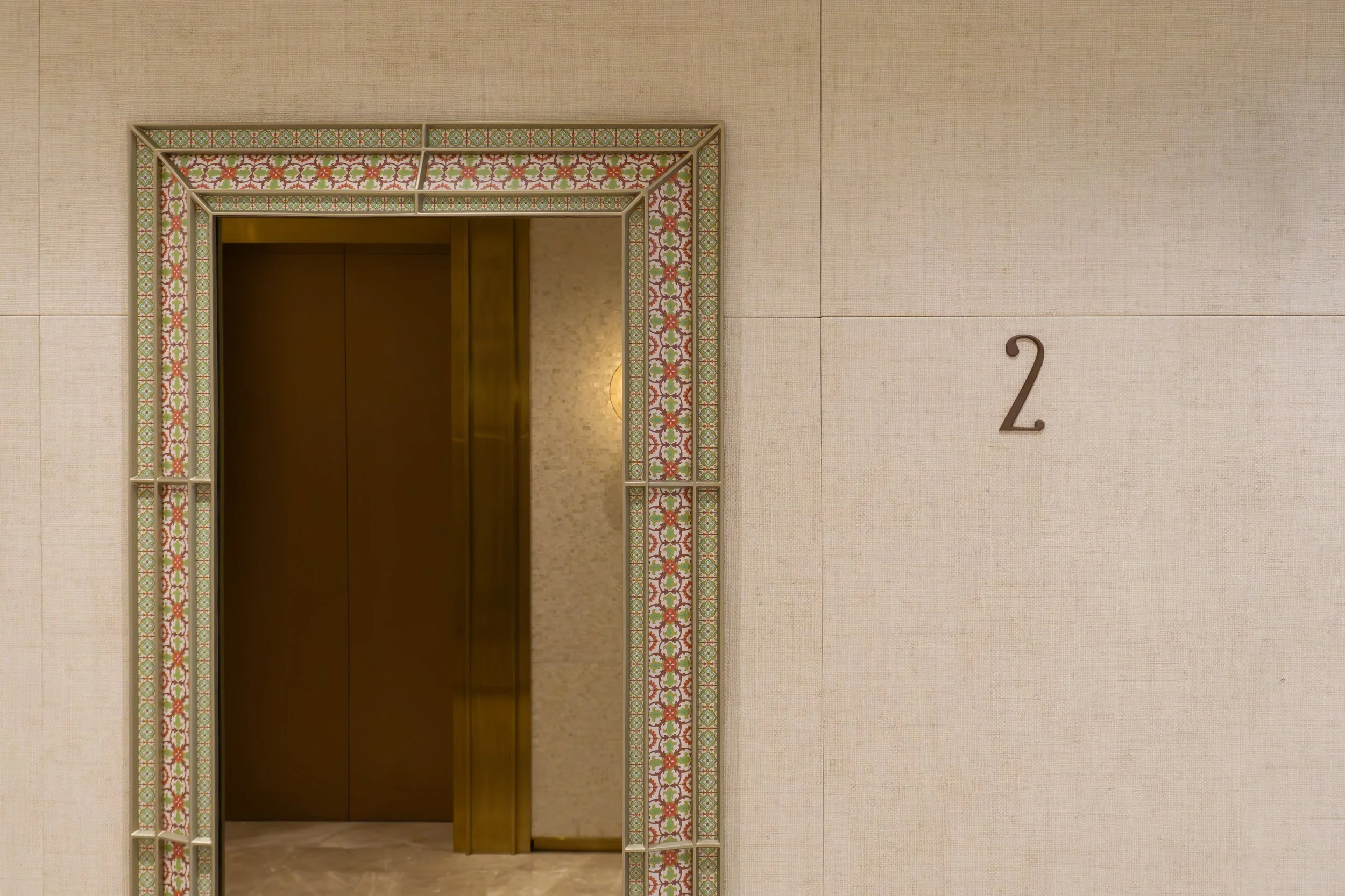 Interior elevator lobby with beige wall, decorative mirror frame, and the number 2 on the wall.