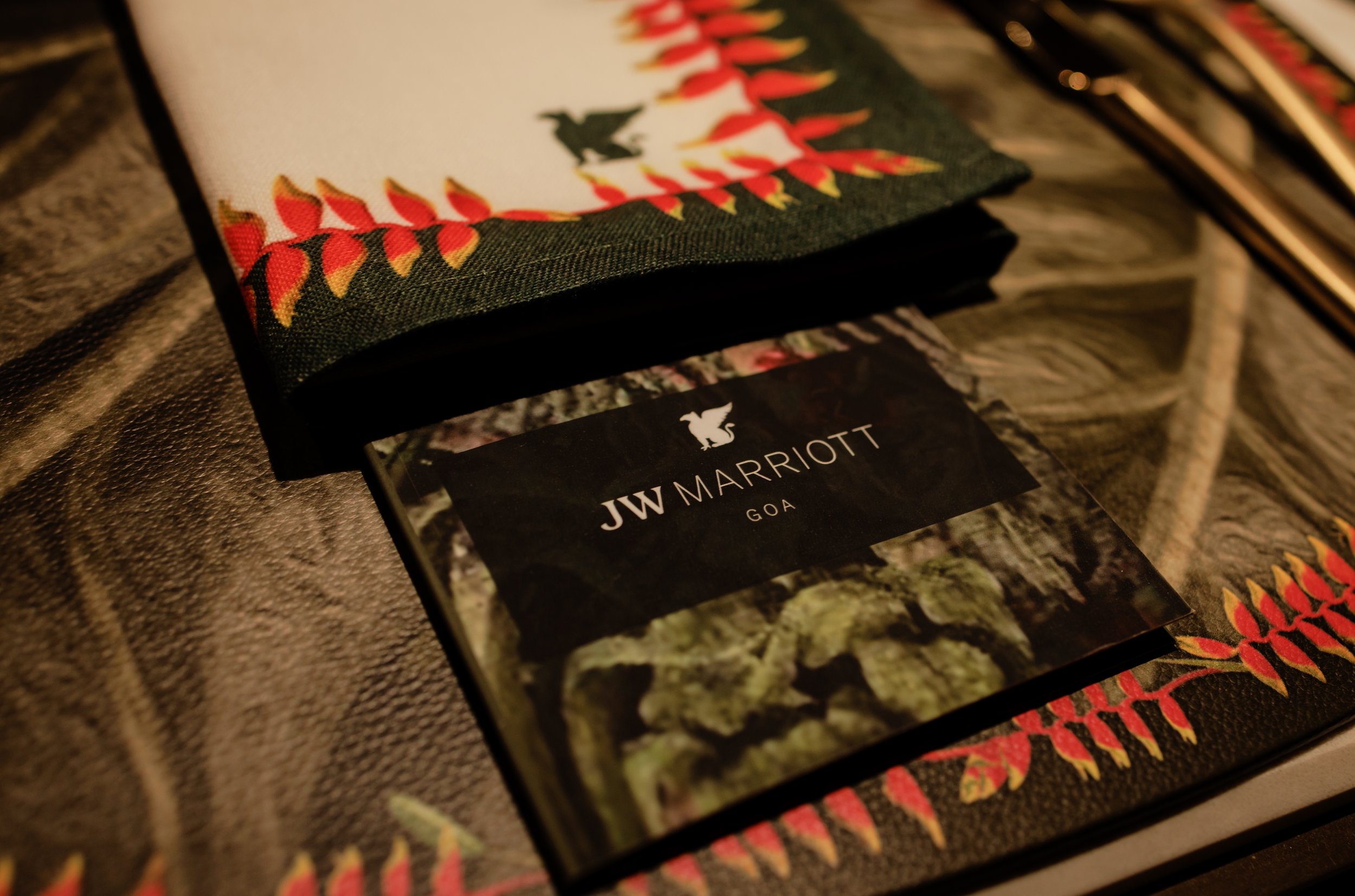A close-up of a folded colorful fabric with a Christmas-themed border, a JW Marriott Goa booklet featuring a dragon logo, and a menu on the right side.