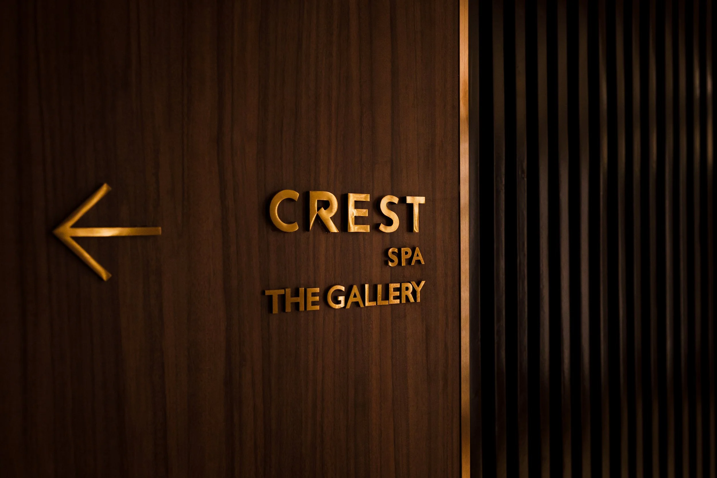 Wood-paneled wall with gold-colored sign indicating direction to Crest Spa and The Gallery, pointing left.