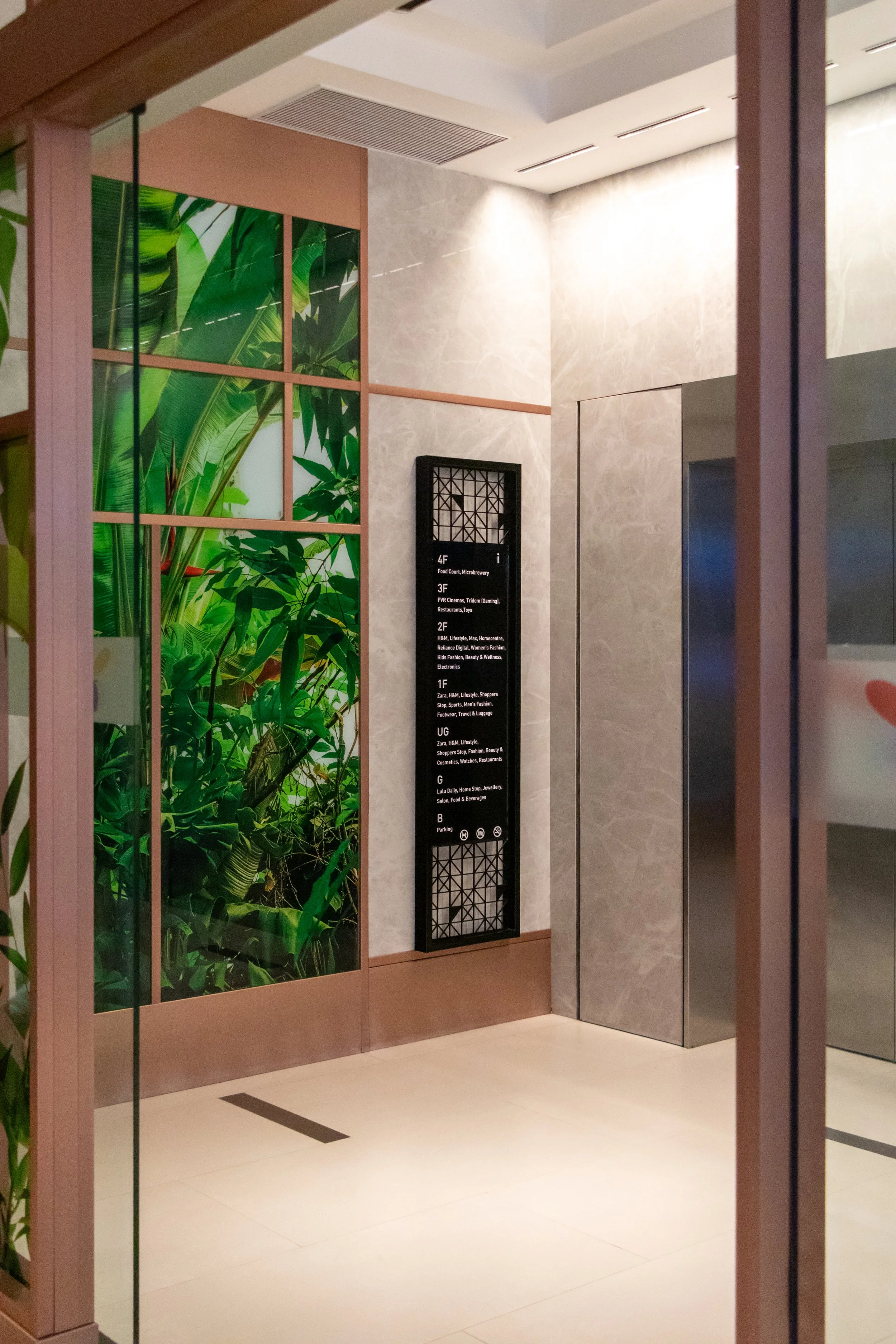 Elevator lobby with a digital directory sign, an elevator door, and a decorative green plant wall.