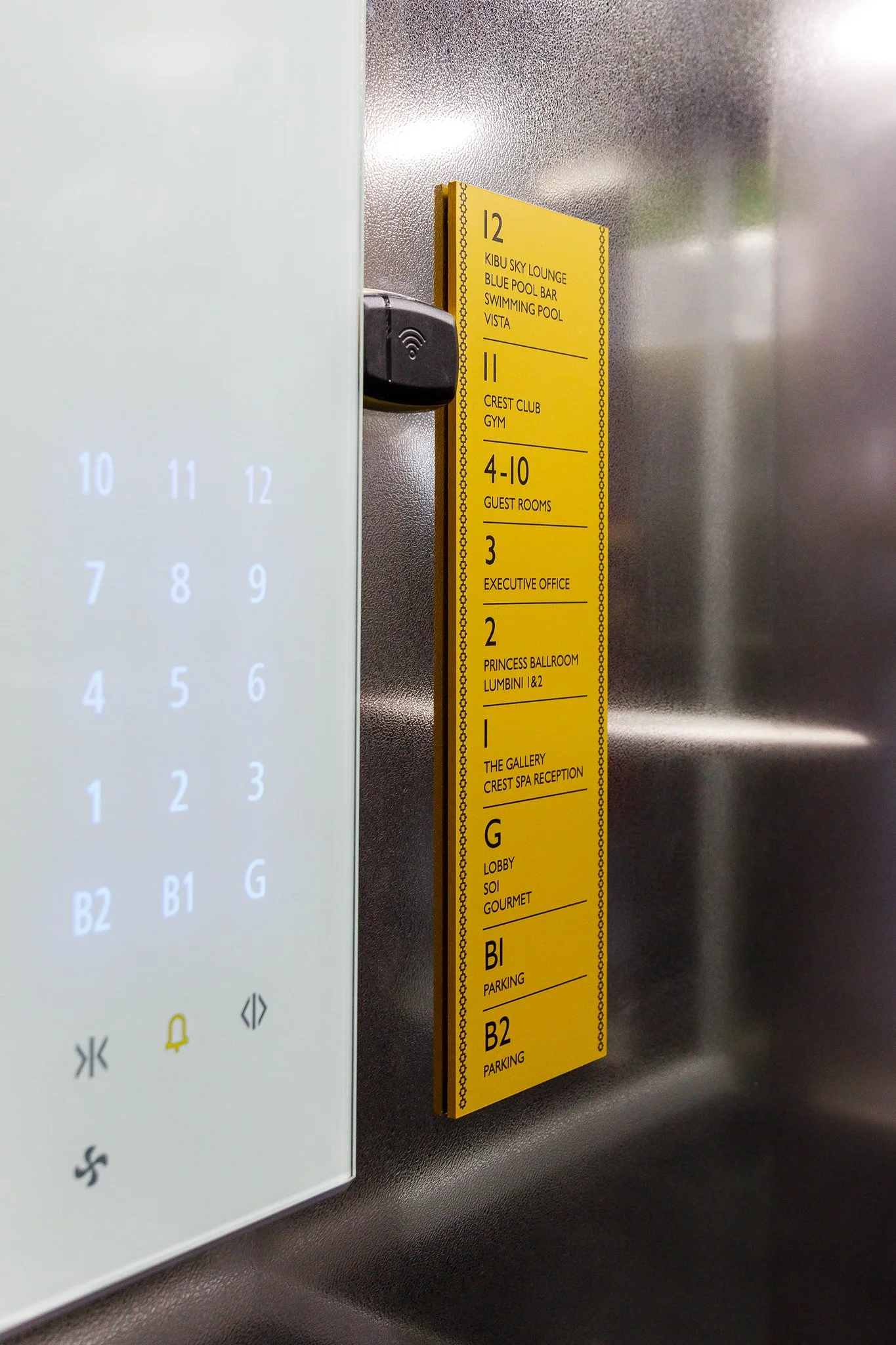 Elevator interior with a yellow directory sign listing hotel amenities and room numbers.