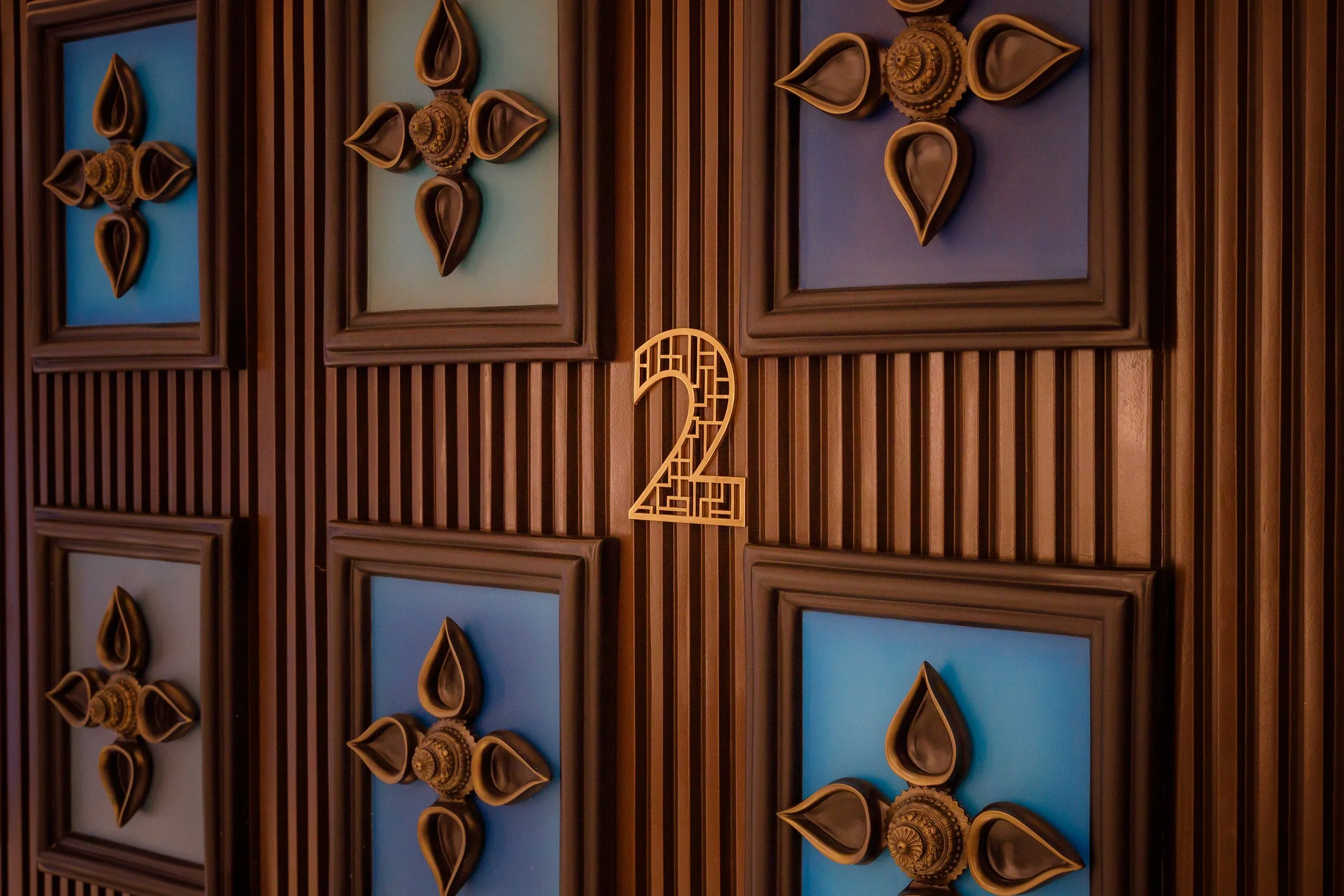 Decorative wall with framed art and a large numbers two and two in gold, set against a background of brown vertical wooden slats.