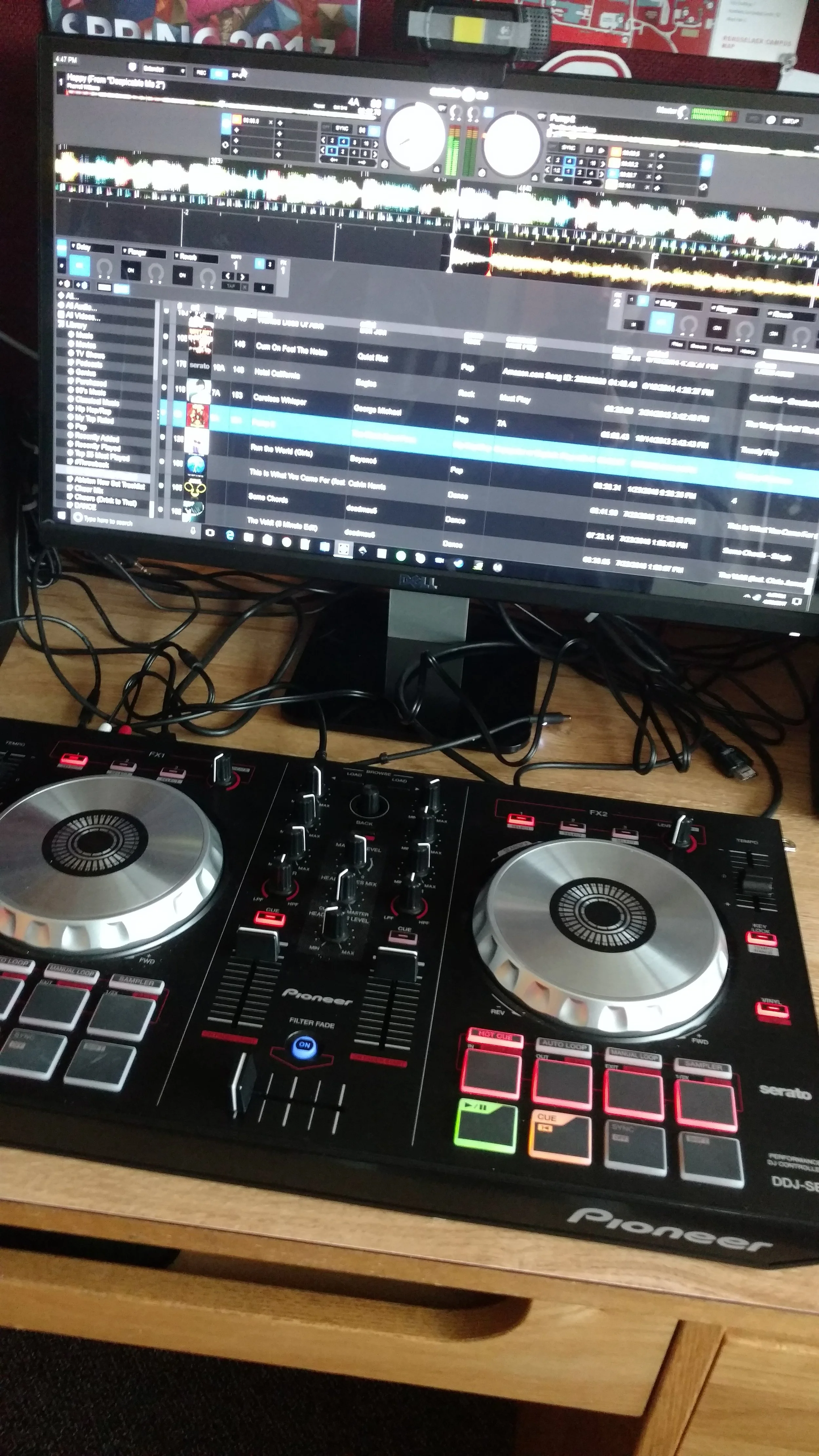 an image of a Pioneer DDJ-SB1 with an assortment of cables behind it, as well as a screen in the background with Serato DJ on the screen, a few tracks "Some Chords" and "The Veldt (8 Minute Edit)" are visible