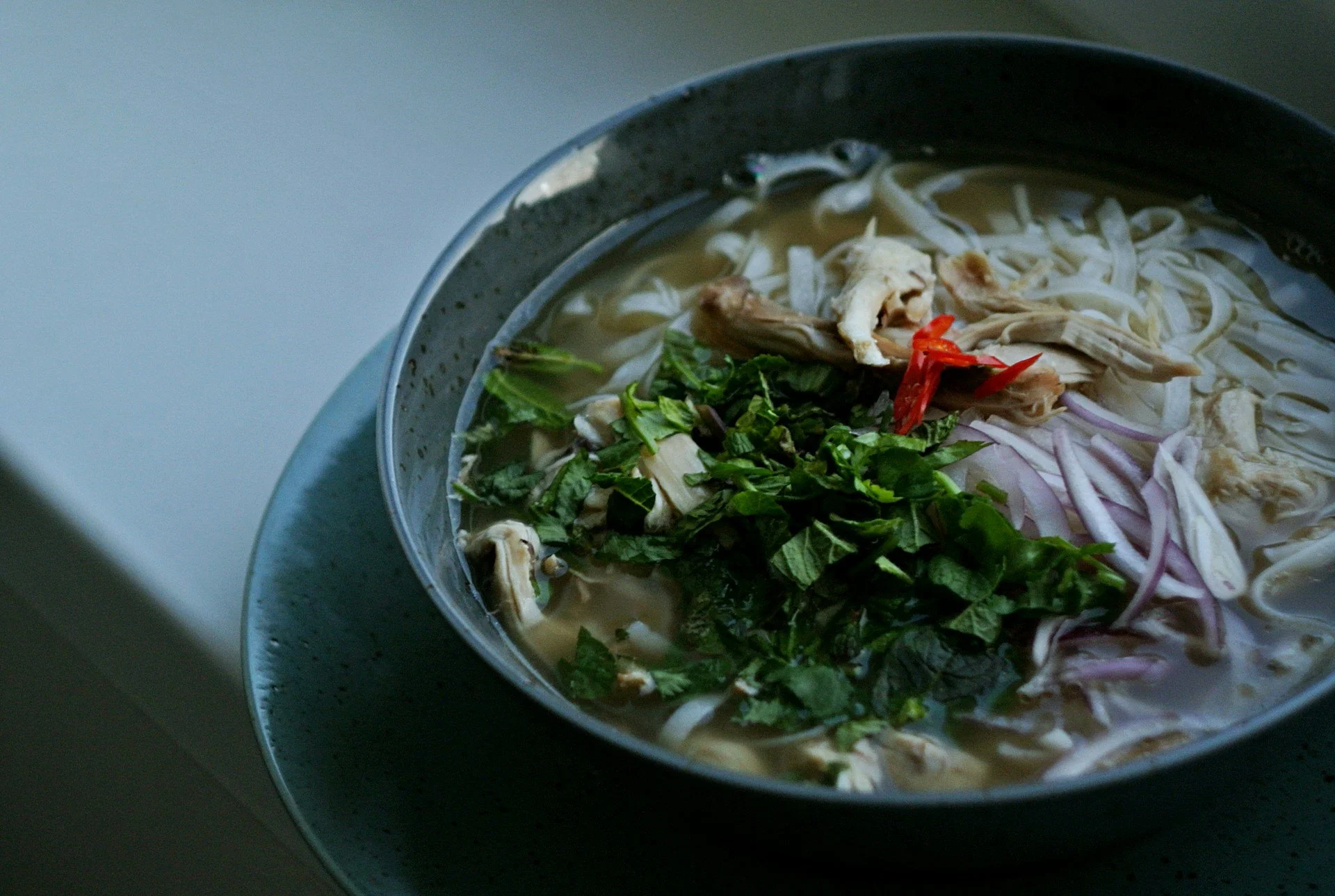 A steaming bowl of Vietnamese pho with herbs and spices in a white bowl, evoking warmth and comfort.