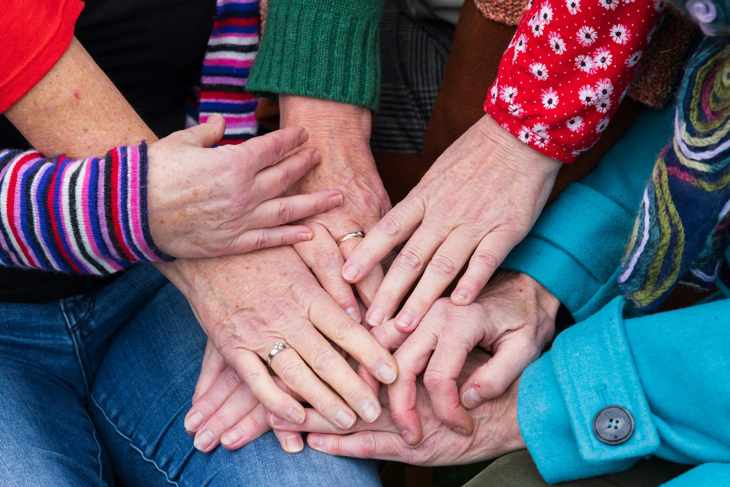 A group of hands gently coming together in a supportive circle over soft, neutral fabric, symbolizing community, care, and holistic healing.