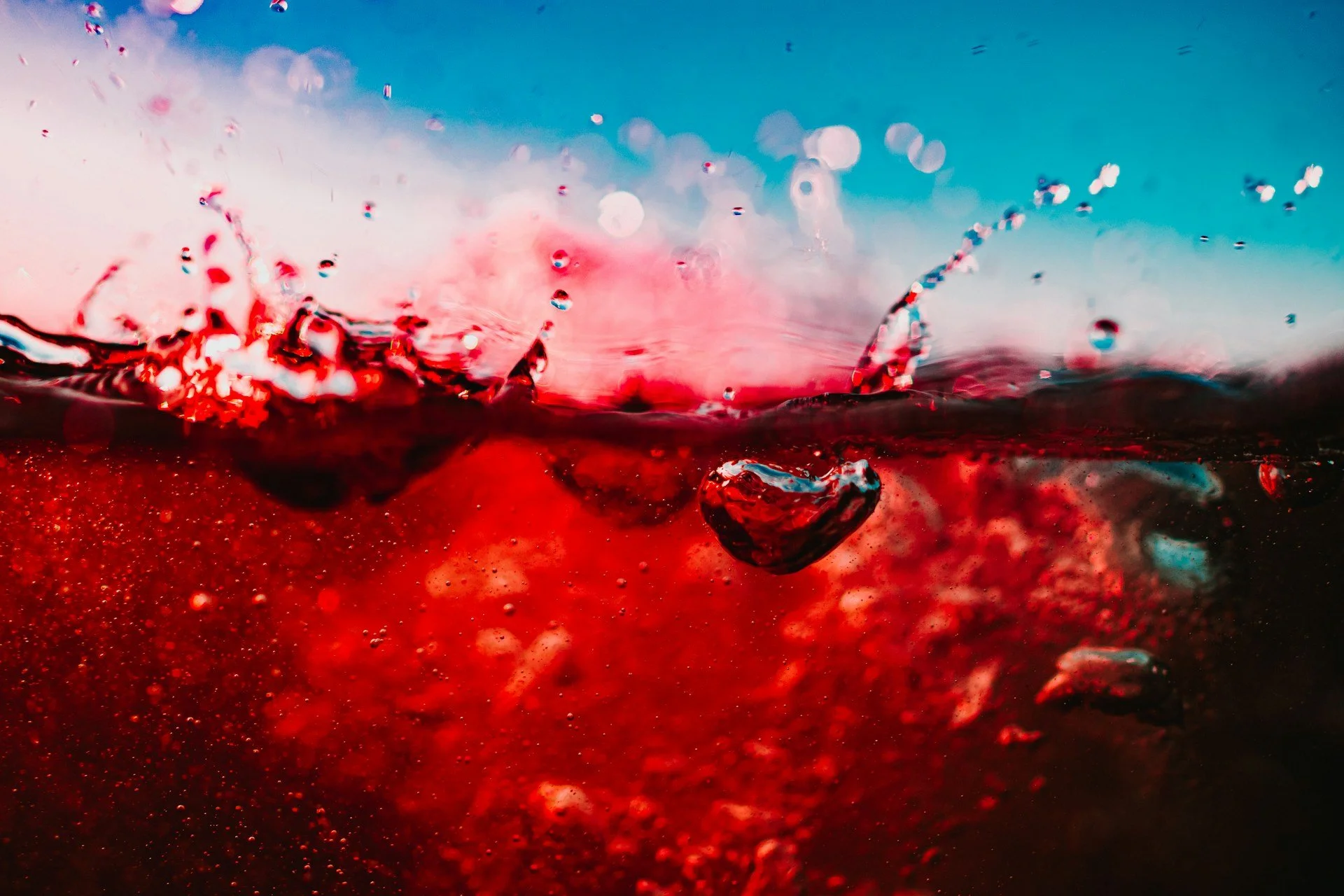 Close-up of red and blue surfaces meeting with droplets of water, symbolizing contrast, fluidity, and the yin-yang balance of seasonal and hormonal cycles