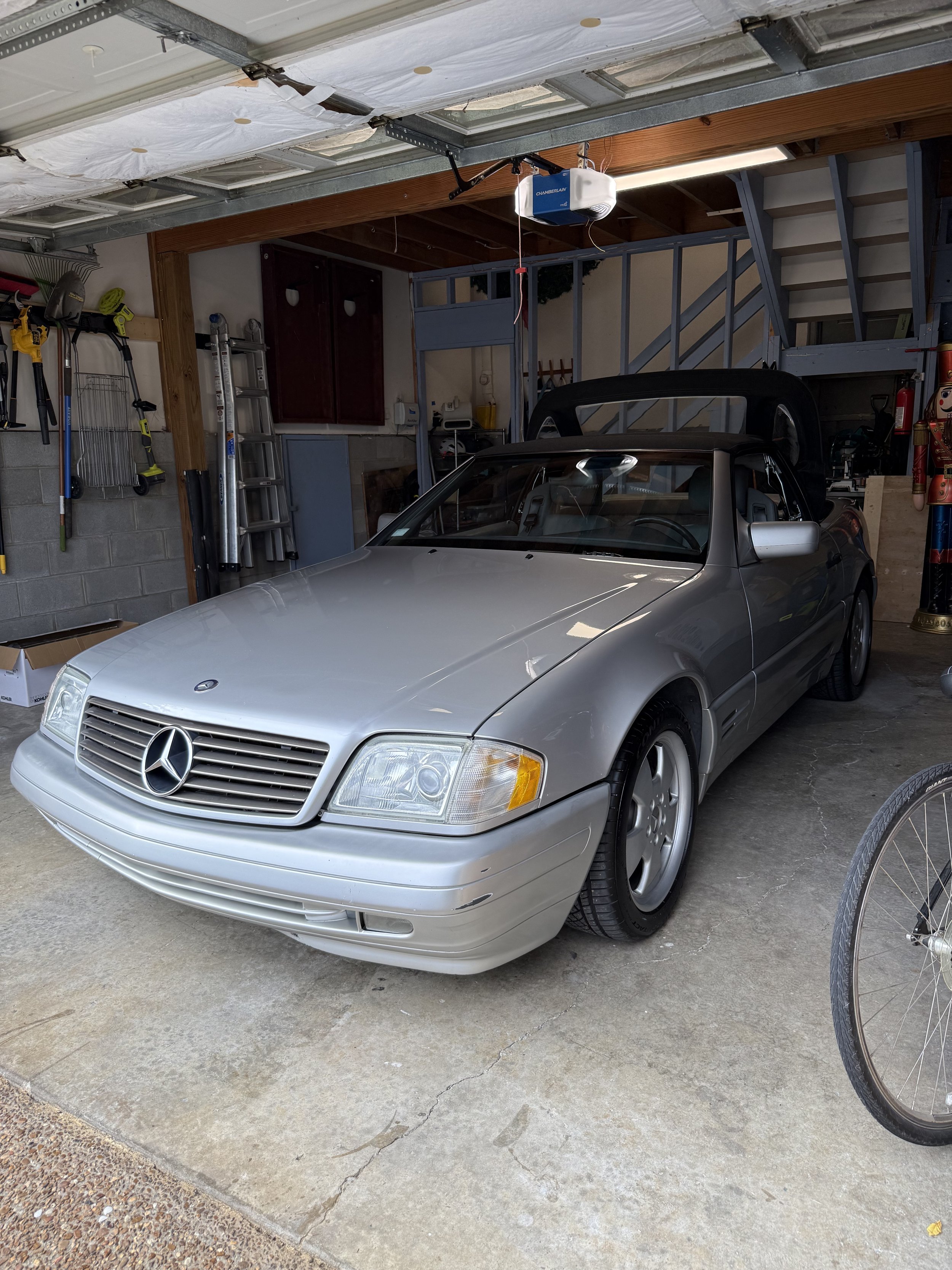 A silver Mercedes-Benz convertible car parked inside a garage with tools and a ladder on the wall.