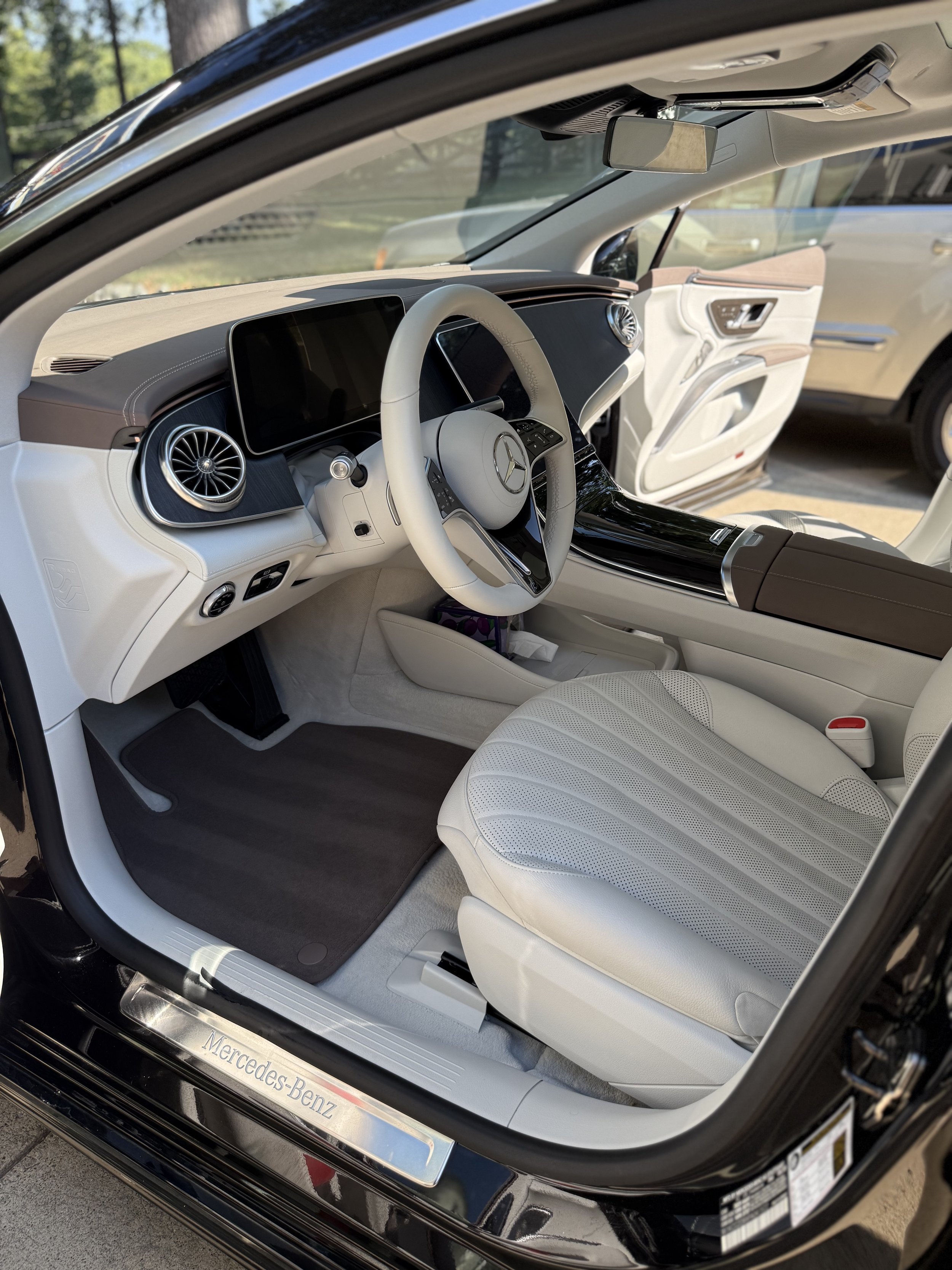 Interior of a luxury Mercedes-Benz electric vehicle with a white steering wheel, digital display, air vents, and light-colored seats.