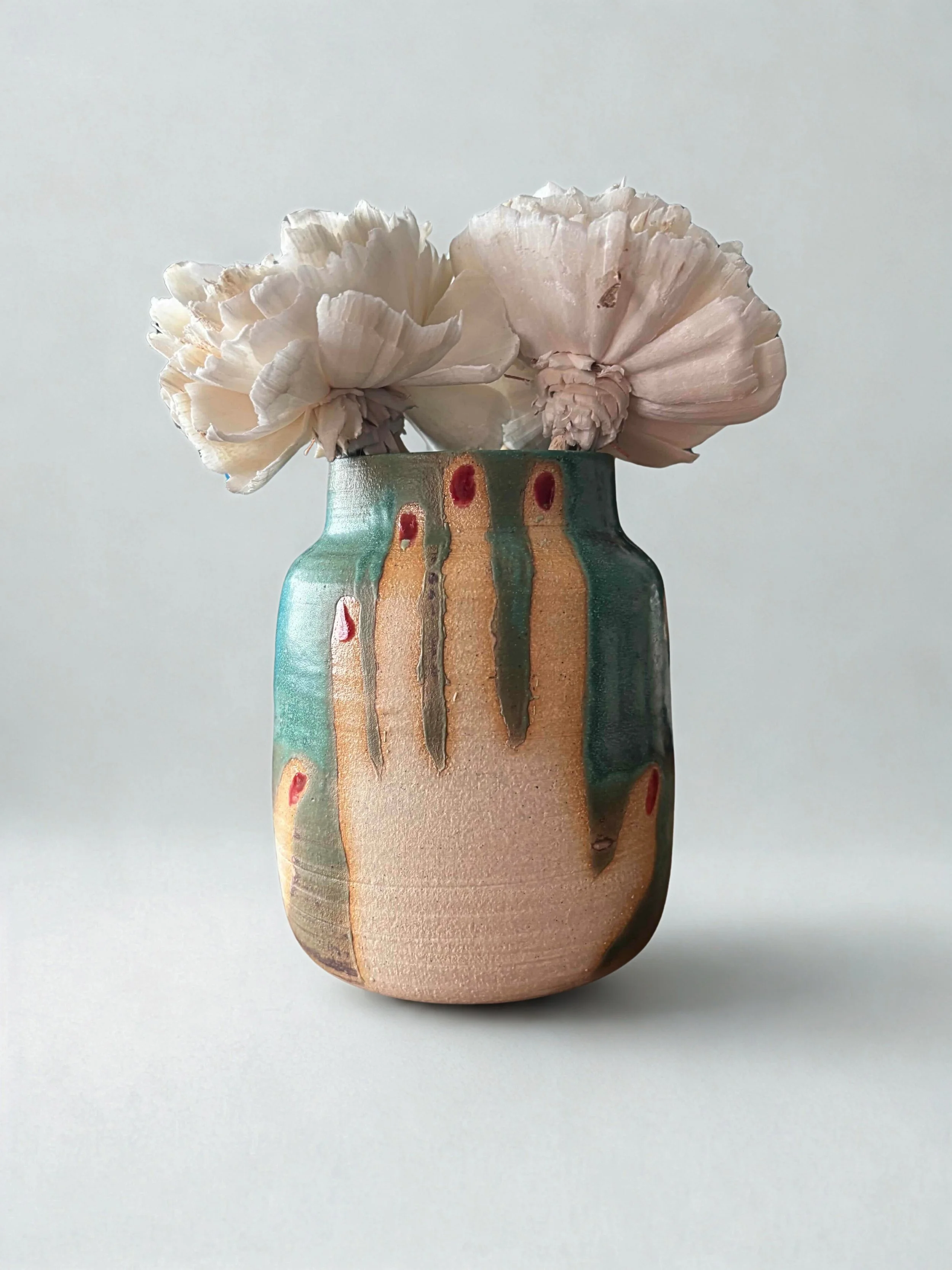 A ceramic vase with a colorful abstract design holding pale pink peony flowers against a plain, light background.
