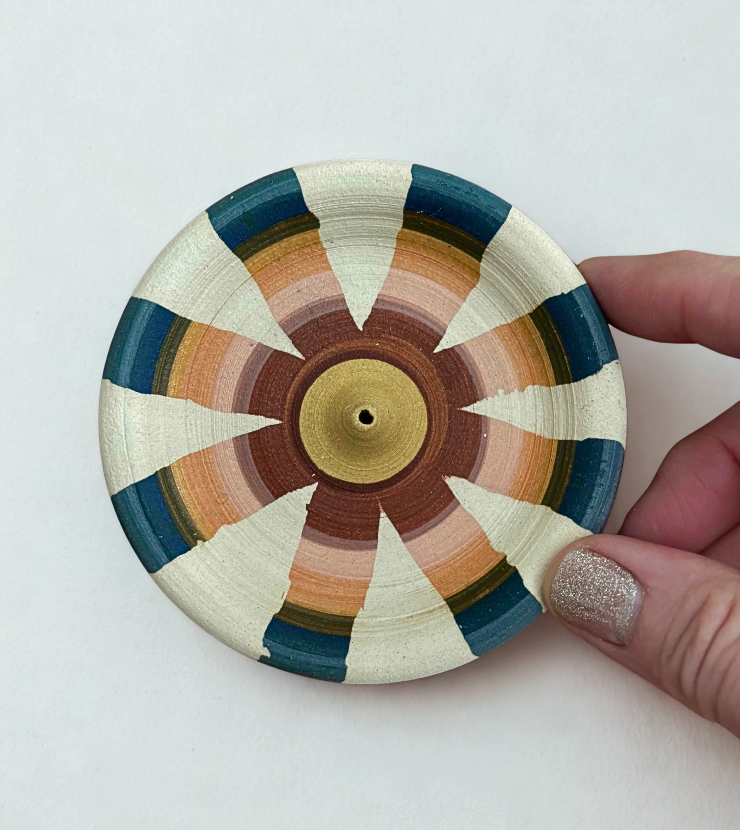 Colorful painted ceramic bowl, with geometric pattern in shades of beige, blue, pink, brown, and green, held by a person with glittery fingernails.
